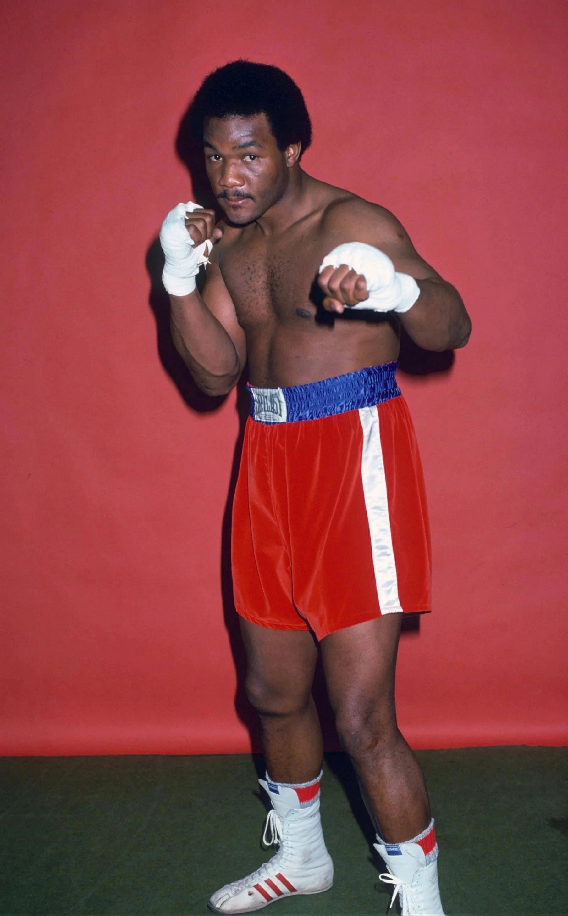 Boxing 桌布 壁紙 — 一位肌肉發達的拳擊手穿著紅色天鵝絨短褲和白色手套，在純紅色背景下擺出戰鬥姿勢。