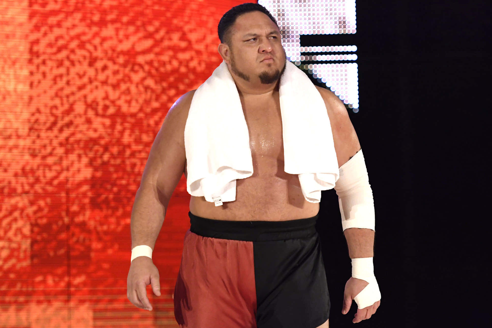 WWE 桌布 壁紙 — 一位肌肉發達的摔角手，肩上披著毛巾，自信地站在發光的紅色數位背景前。