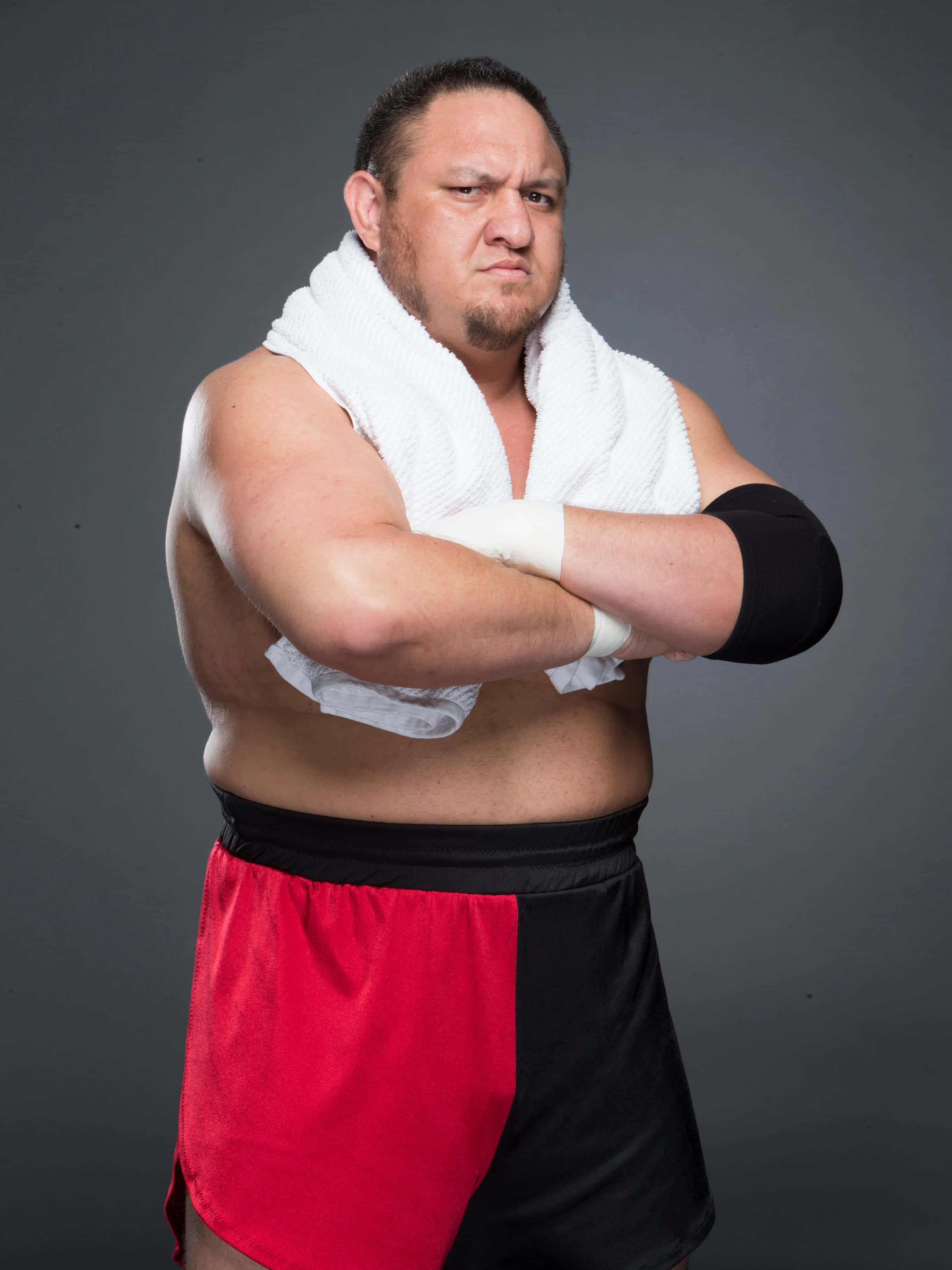 WWE 桌布 壁紙 — 一位肌肉發達的摔角手，肩上披著毛巾，雙臂交叉，站在灰色攝影棚背景前。