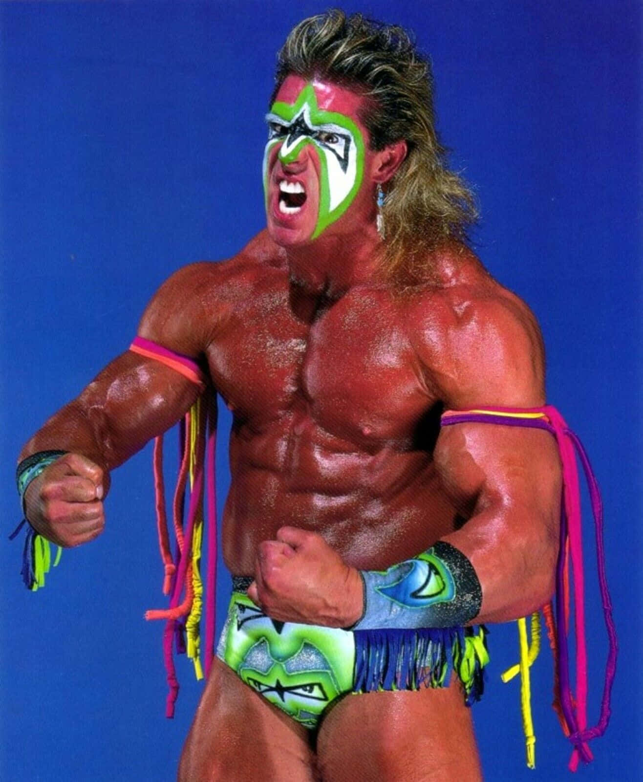 WWE 桌布 壁紙 — 一位肌肉發達的摔角手，臉上塗著綠色和白色的顏料，在純藍色背景前咆哮。
