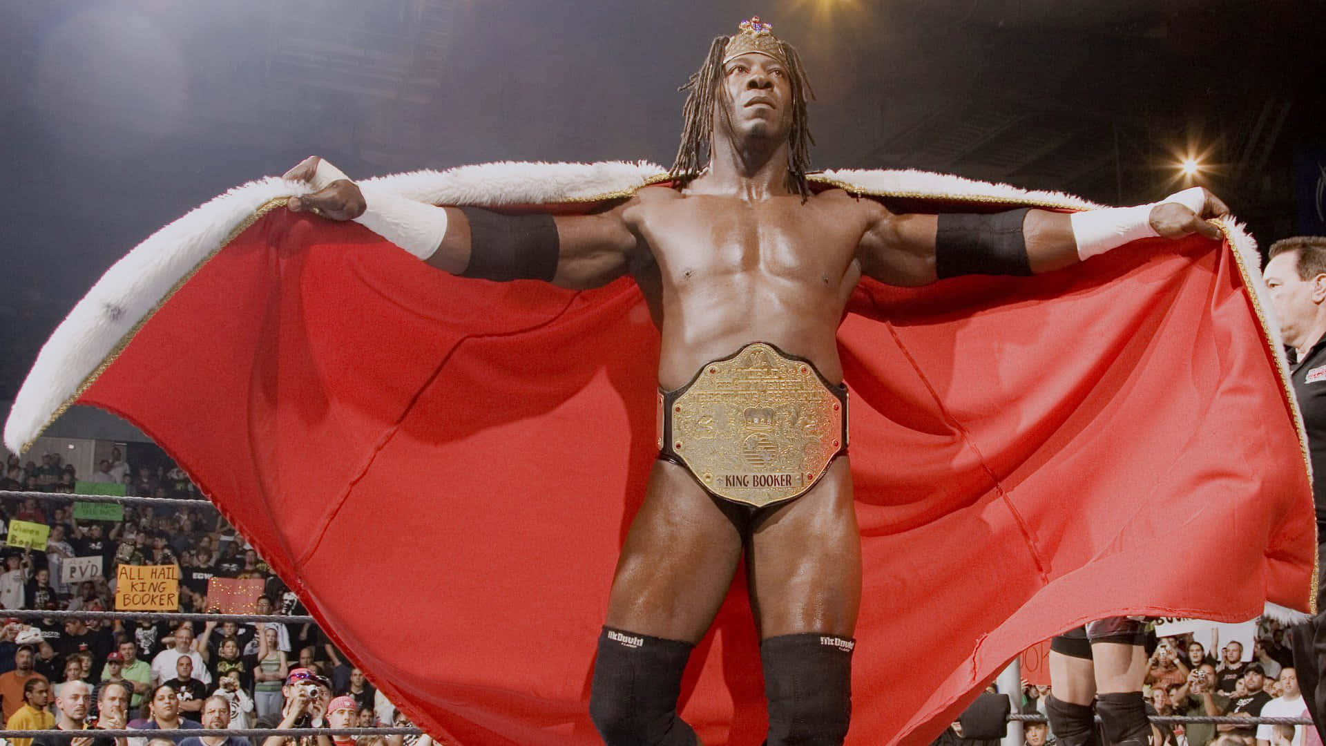 WWE 桌布 壁紙 — 一位肌肉發達的摔角手，身穿紅色披風和冠軍腰帶，在擂台上勝利地站立，背後是咆哮的人群。