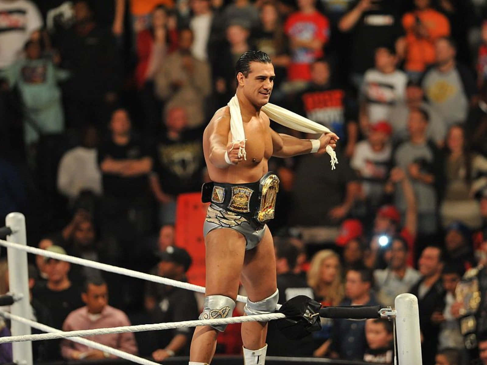 WWE 桌布 壁紙 — 一位肌肉發達的摔角手，身穿銀色短褲和冠軍腰帶，在擂台上勝利地站著，手持白色毛巾。