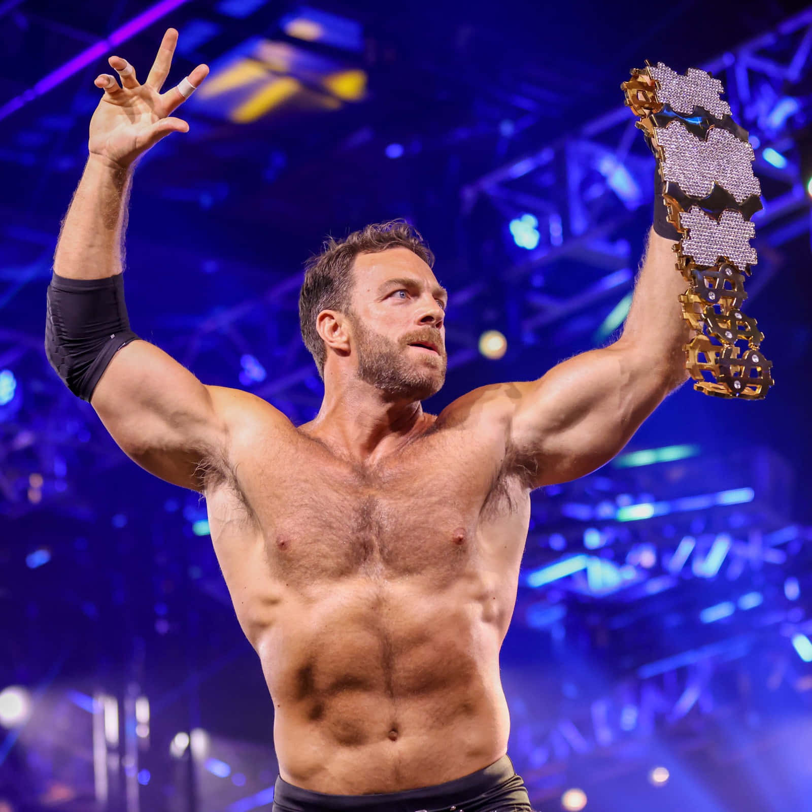 WWE 桌布 壁紙 — 一位肌肉發達的摔角手在充滿活力的藍色舞台燈光下勝利地高舉閃閃發光的冠軍腰帶。