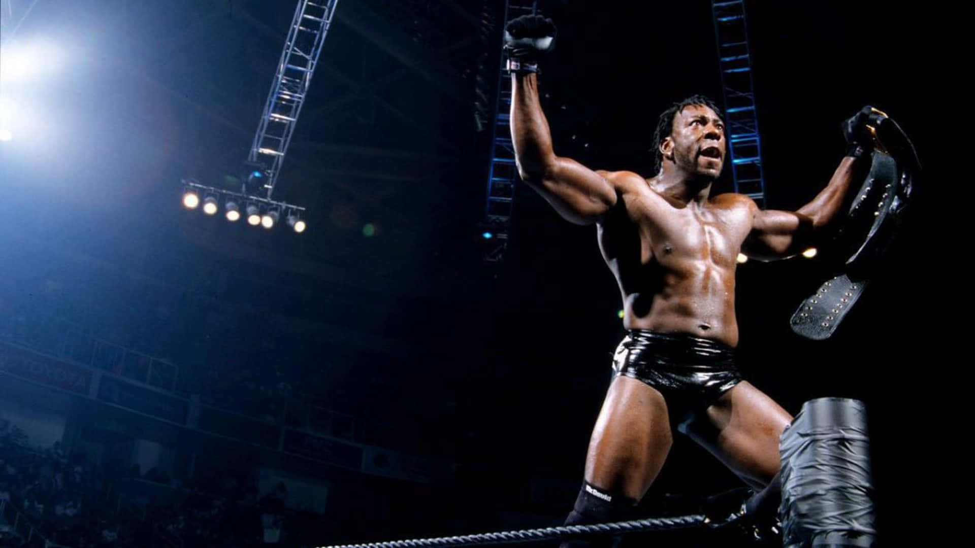 WWE 桌布 壁紙 — 一位肌肉發達的摔角手在場館燈光下，於明亮照明的擂台上勝利地高舉雙臂和冠軍腰帶。