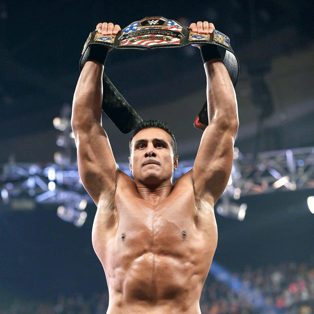 WWE 桌布 壁紙 — 一位肌肉發達的摔角手在場館燈光下高舉冠軍腰帶慶祝勝利。