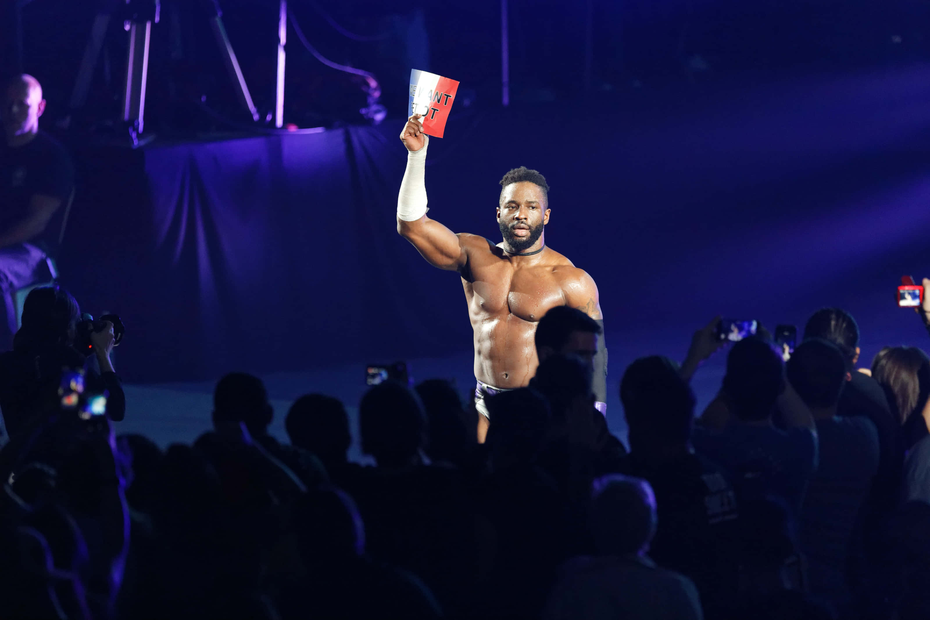WWE 桌布 壁紙 — 一位肌肉發達的摔角手在擂台上，在戲劇性的紫色舞台燈光下，向歡呼的人群舉起紅牌。