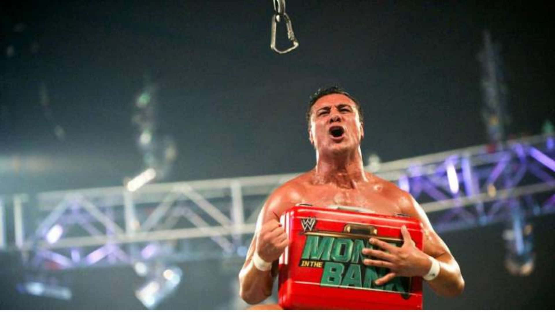 WWE 桌布 壁紙 — 一位肌肉發達的摔角手在明亮的場館燈光下，高舉紅色「Money in the Bank」公事包，發出勝利的吶喊。
