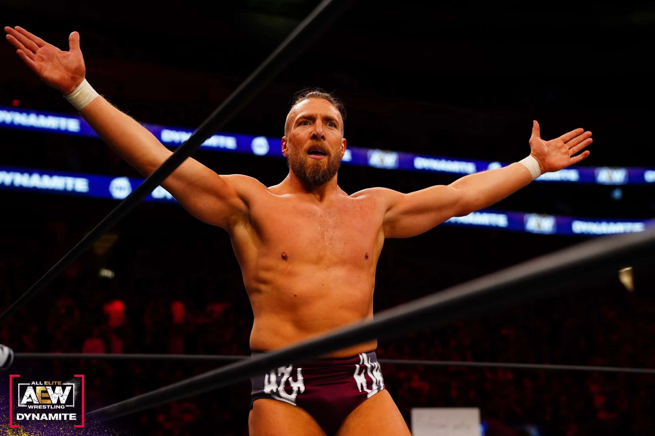 WWE 桌布 壁紙 — 一位肌肉發達的摔角手張開雙臂，在明亮的競技場燈光下於摔角場內勝利慶祝。
