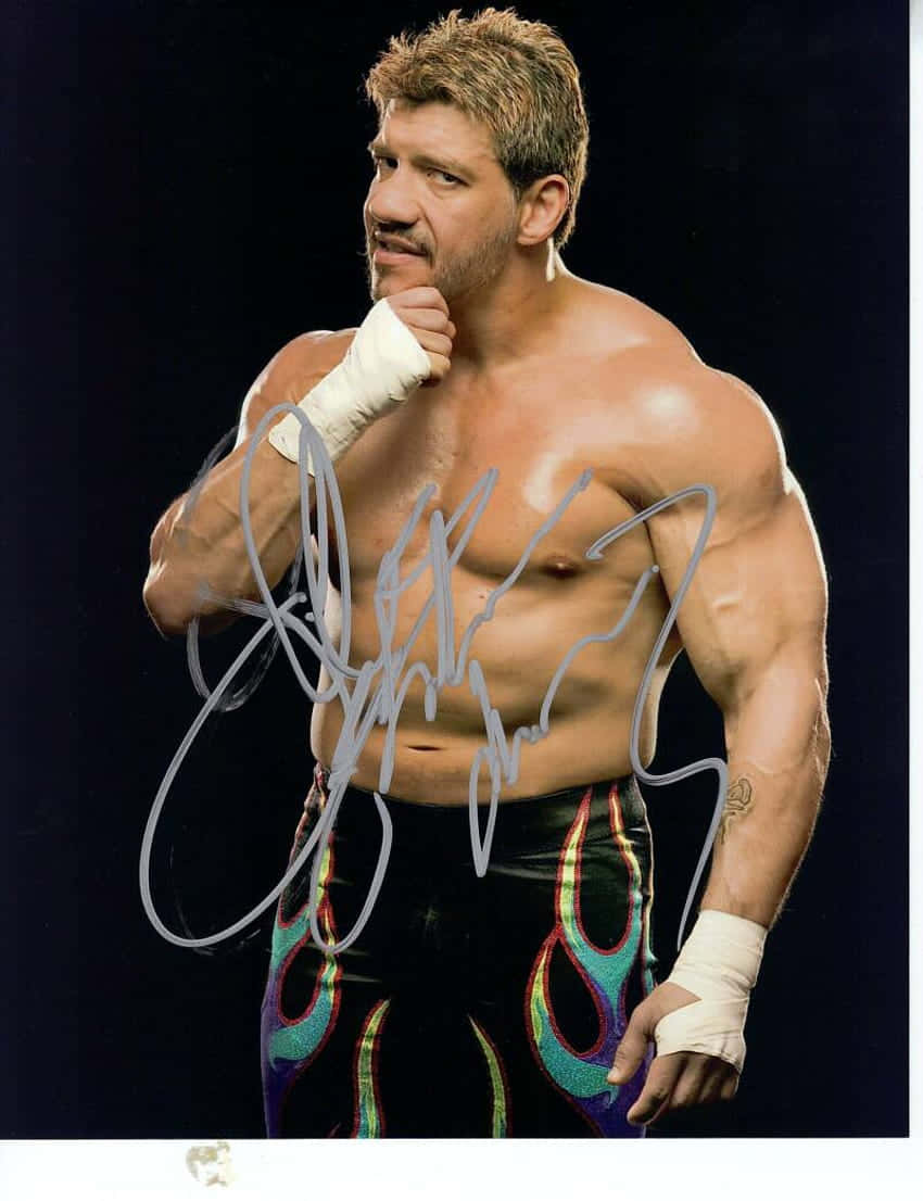 Wrestling 桌布 壁紙 — 一位肌肉發達的摔角手穿著彩色火焰圖案三角褲和白色護腕，在黑色背景前自信地擺姿勢，並帶有簽名疊加。