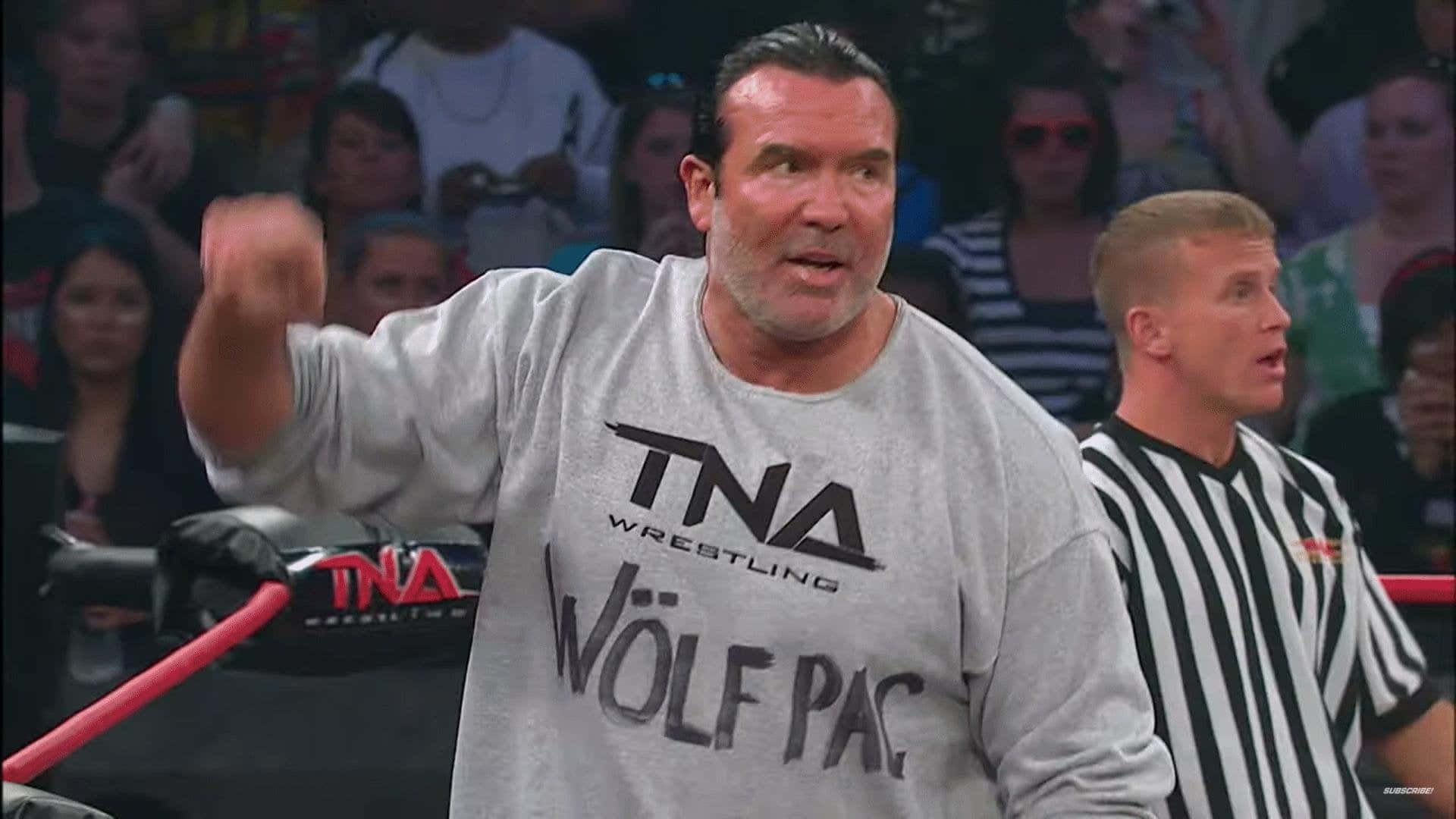 WWE 桌布 壁紙 — 一位肌肉發達的摔角手穿著灰色 'TNA WOLF PAC' T恤，在裁判注視下於擂台上揮拳。