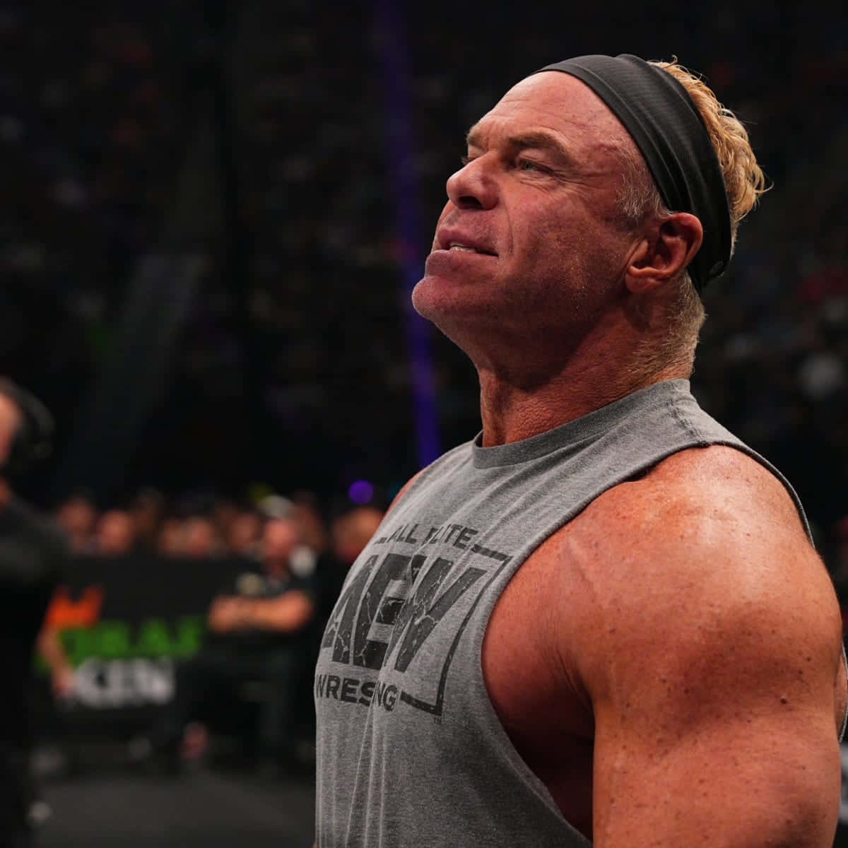 WWE 桌布 壁紙 — 一位肌肉發達的摔角手穿著灰色背心和黑色頭帶，在燈光昏暗的競技場中專注地向上看。