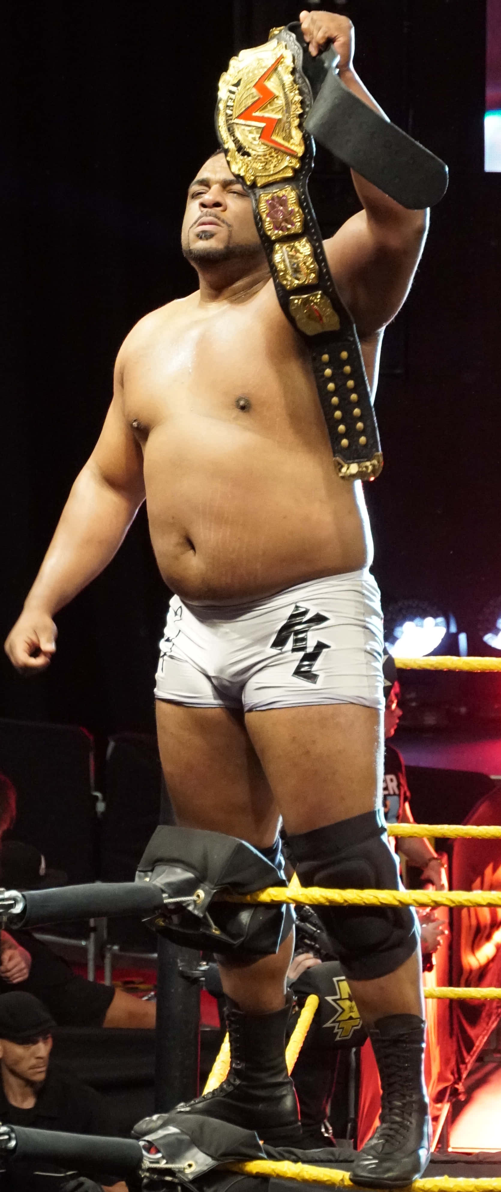 WWE 桌布 壁紙 — 一位肌肉發達的摔角手穿著白色緊身褲，在擂台上勝利地高舉金色冠軍腰帶。