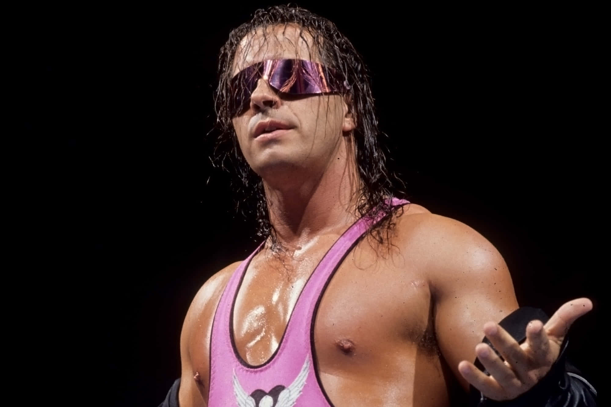 WWE 桌布 壁紙 — 一位肌肉發達的摔角手穿著粉紅色緊身衣和反光太陽眼鏡，濕髮，張開手掌，自信地站在黑色背景前。