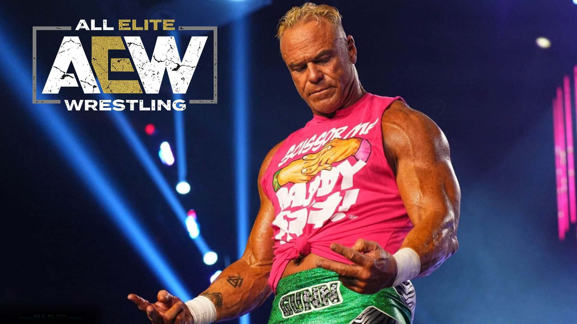 WWE 桌布 壁紙 — 一位肌肉發達的摔角手穿著粉紅色背心和綠色短褲，在藍色舞台燈光下擺姿勢，AEW標誌清晰可見。