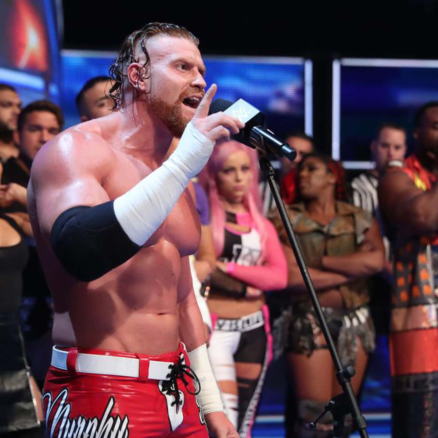 WWE 桌布 壁紙 — 一位肌肉發達的摔角手穿著紅色短褲，在現場活動中對著麥克風大喊，同時指向人群。