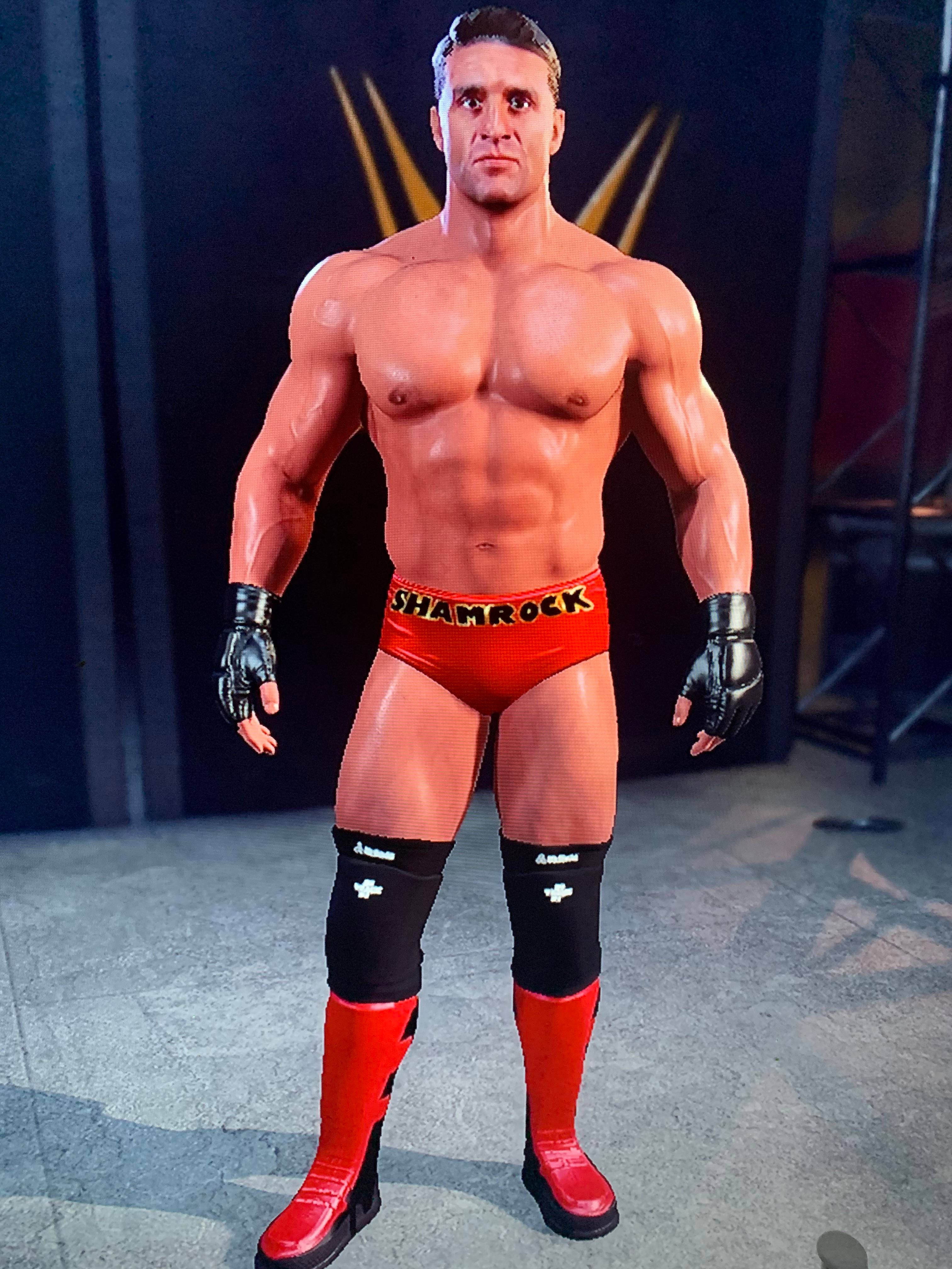 WWE 桌布 壁紙 — 一位肌肉發達的摔角手穿著紅色短褲，上面有'SHAMROCK'字樣，自信地站在黑暗的競技場中，身後有金色舞台燈光。
