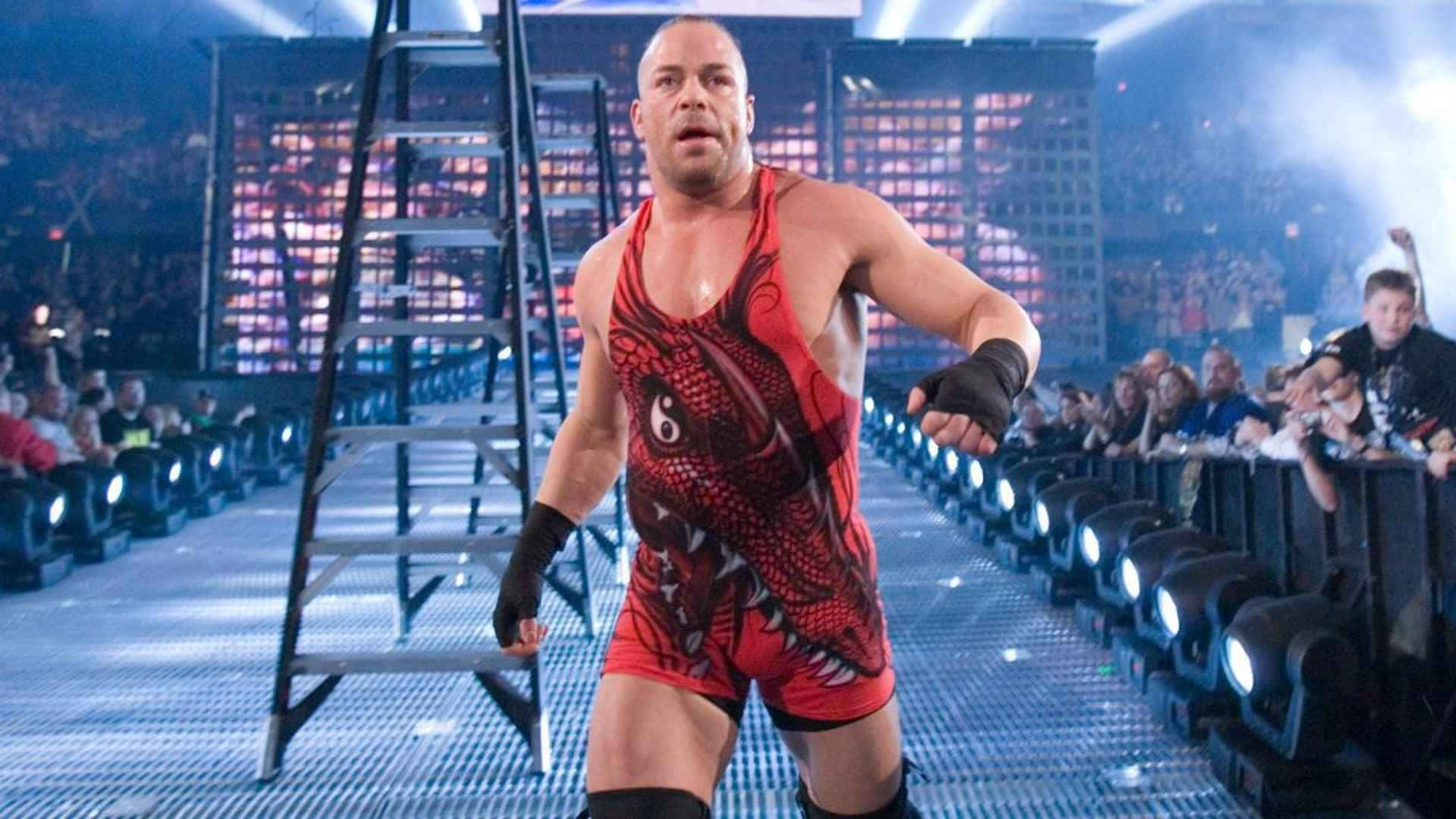 WWE 桌布 壁紙 — 一位肌肉發達的摔角手穿著紅色龍主題緊身衣，自信地走下一條燈火通明的競技場坡道，旁邊放著一把梯子。