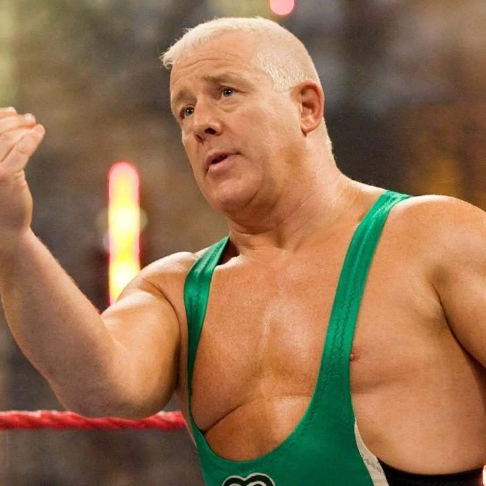 WWE 桌布 壁紙 — 一位肌肉發達的摔角手穿著綠色緊身衣，在明亮的場館燈光下於擂台上舉起拳頭。