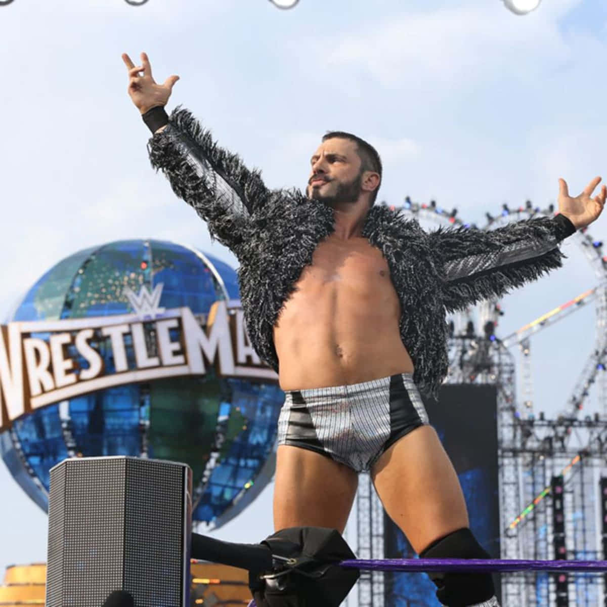 Ring 桌布 壁紙 — 一位肌肉發達的摔角手穿著羽毛外套和閃亮短褲，在WrestleMania的擂台角柱頂端擺出勝利姿勢。