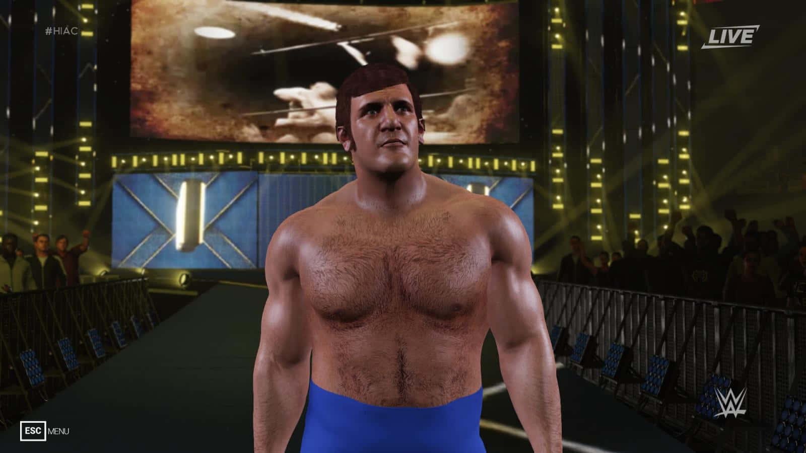 WWE 桌布 壁紙 — 一位肌肉發達的摔角手穿著藍色短褲，在明亮的競技場燈光下站在舞台中央，身後有歡呼的人群。