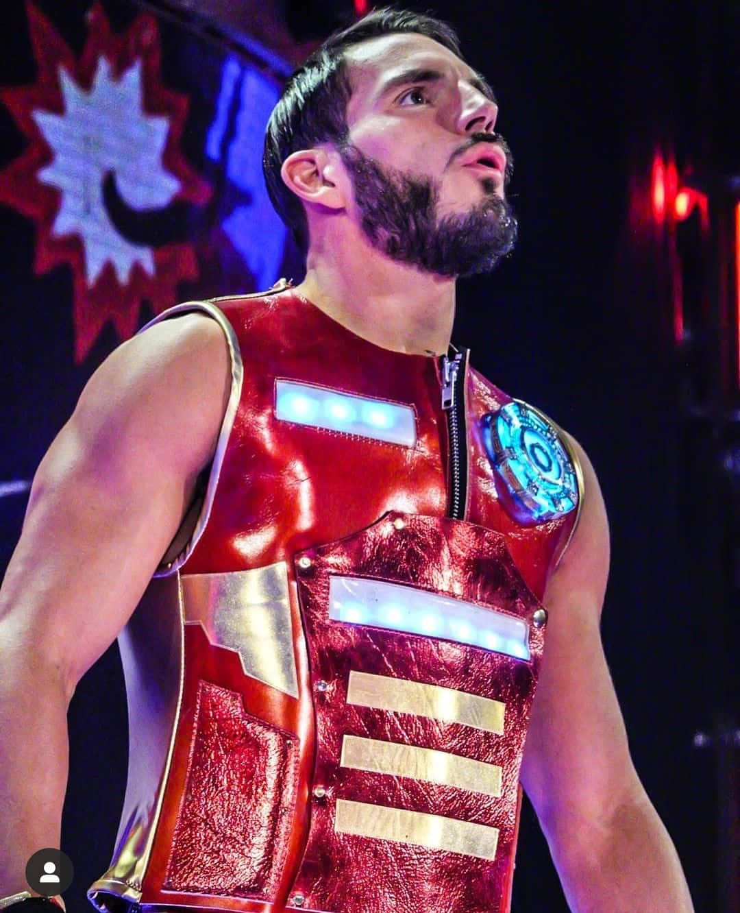 WWE 桌布 壁紙 — 一位肌肉發達的摔角手穿著閃亮的紅金色鋼鐵人風格服裝，帶有發光的藍色點綴，在舞台燈光下自信地站立。