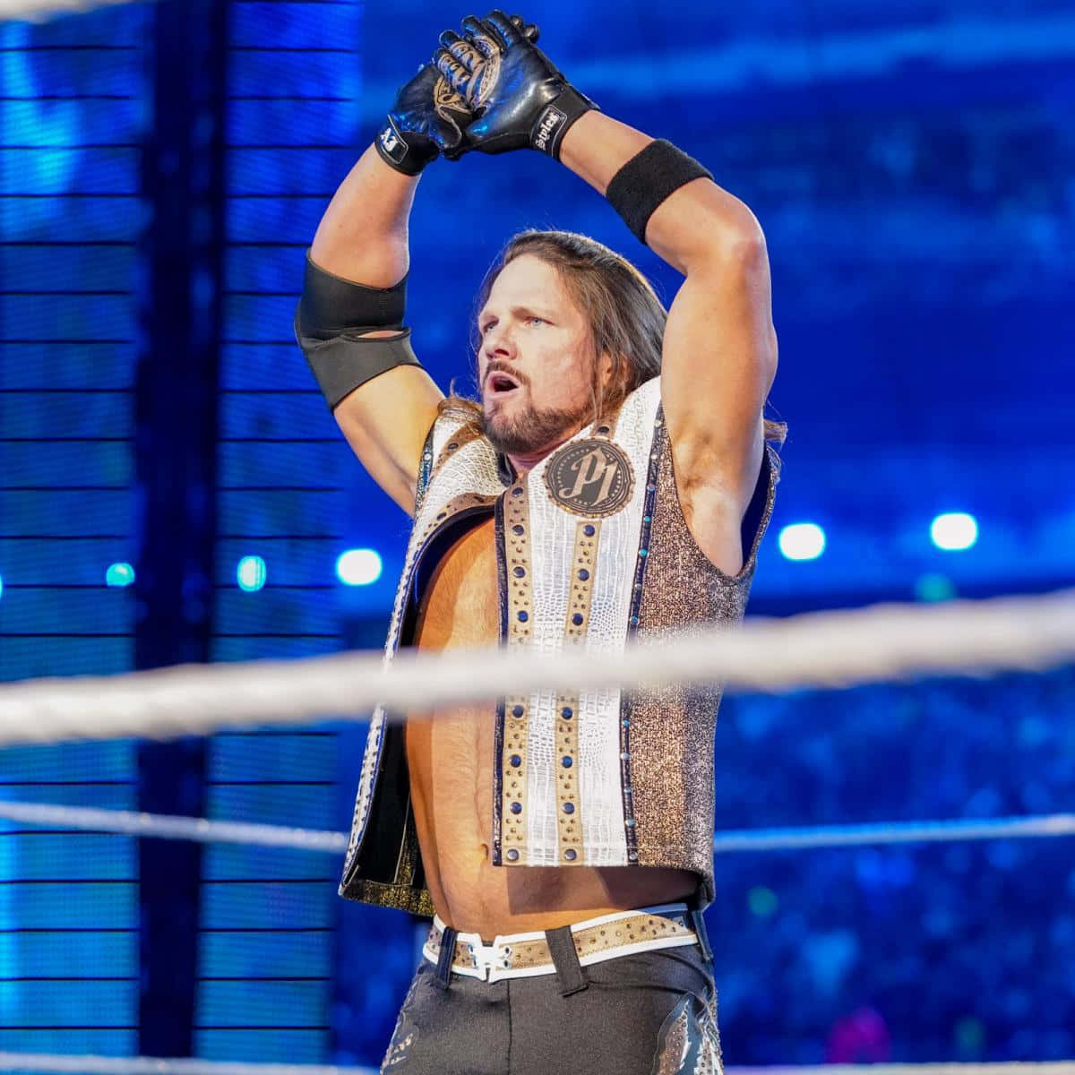 WWE 桌布 壁紙 — 一位肌肉發達的摔角手穿著閃閃發光的背心，在燈光明亮的擂台上舉起戴著手套的雙手慶祝勝利。