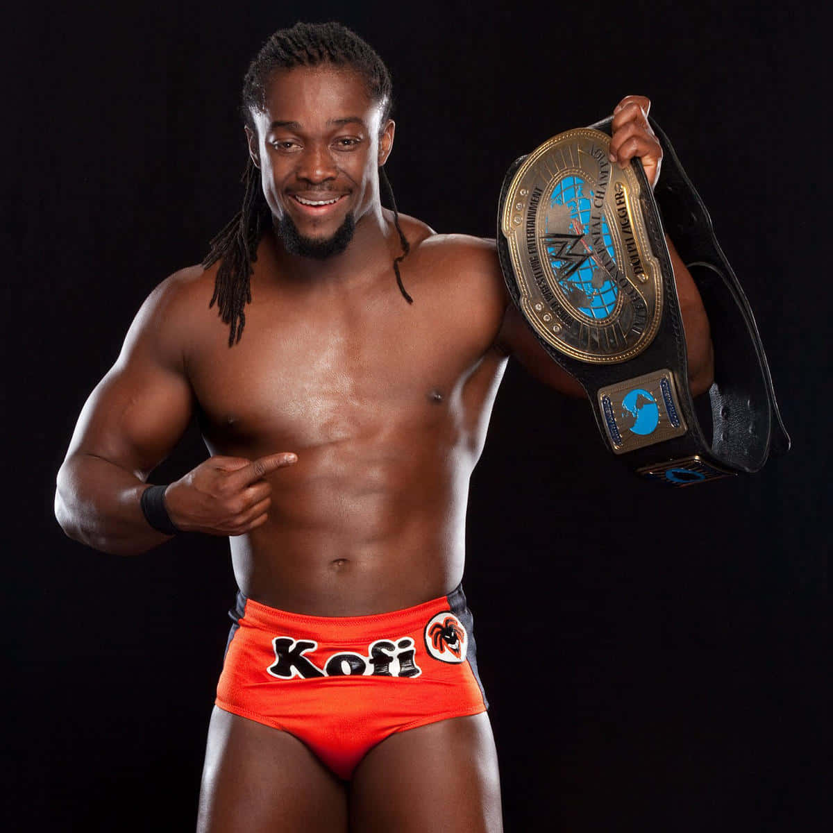 WWE 桌布 壁紙 — 一位肌肉發達的摔角手穿著鮮橙色短褲，在黑色背景前自豪地舉起冠軍腰帶。