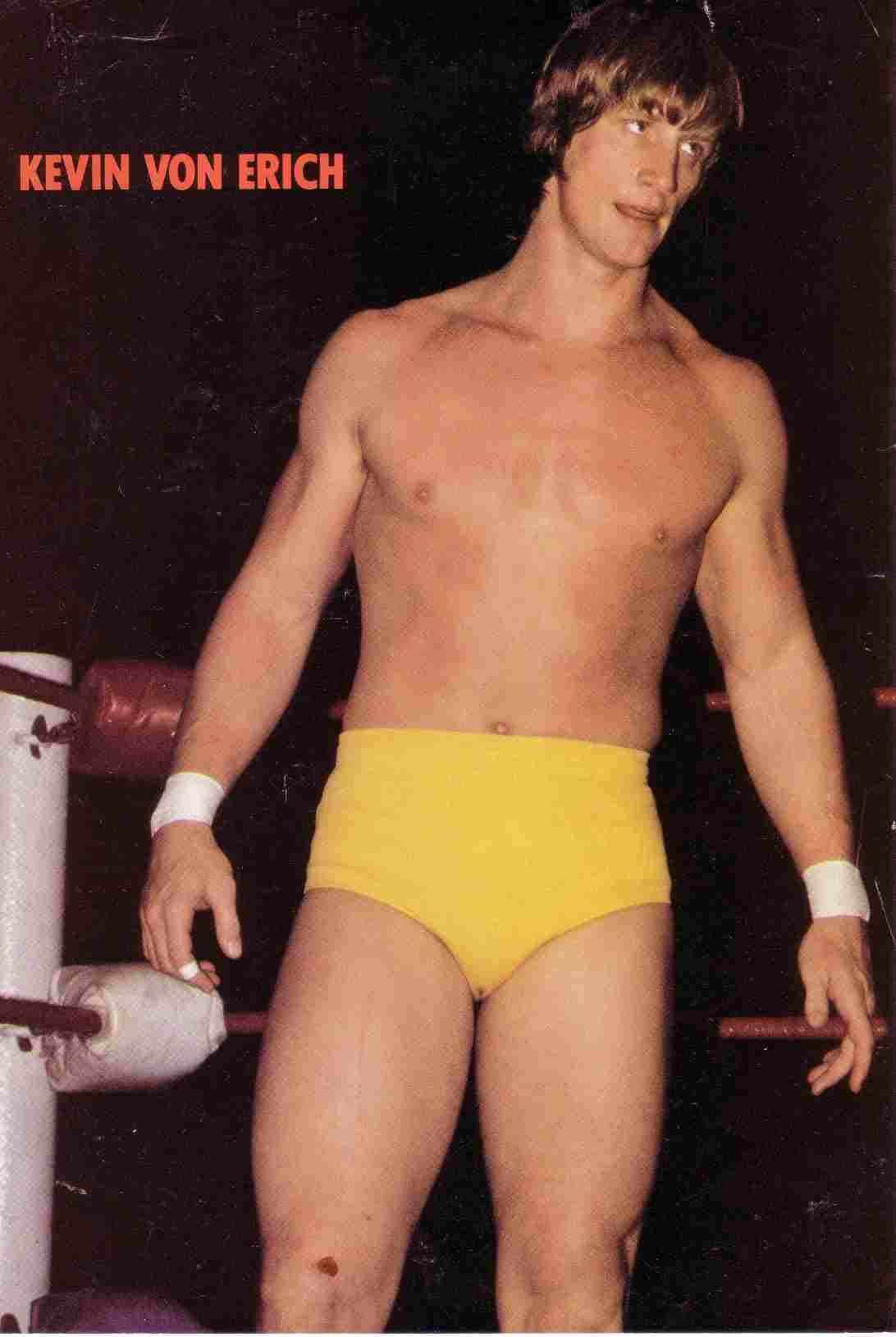 Wrestling 桌布 壁紙 — 一位肌肉發達的摔角手穿著鮮黃色短褲，自信地站在一個有白色繩索和紅色襯墊的擂台內。