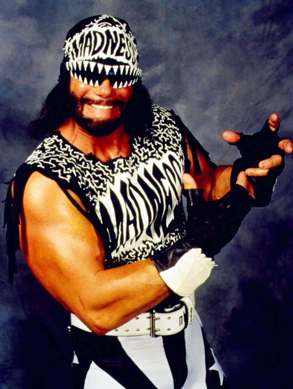 WWE 桌布 壁紙 — 一位肌肉發達的摔角手穿著黑白斑馬紋服裝，戴著寫有「madness」的頭帶，在黑暗的攝影棚背景下自信地微笑。