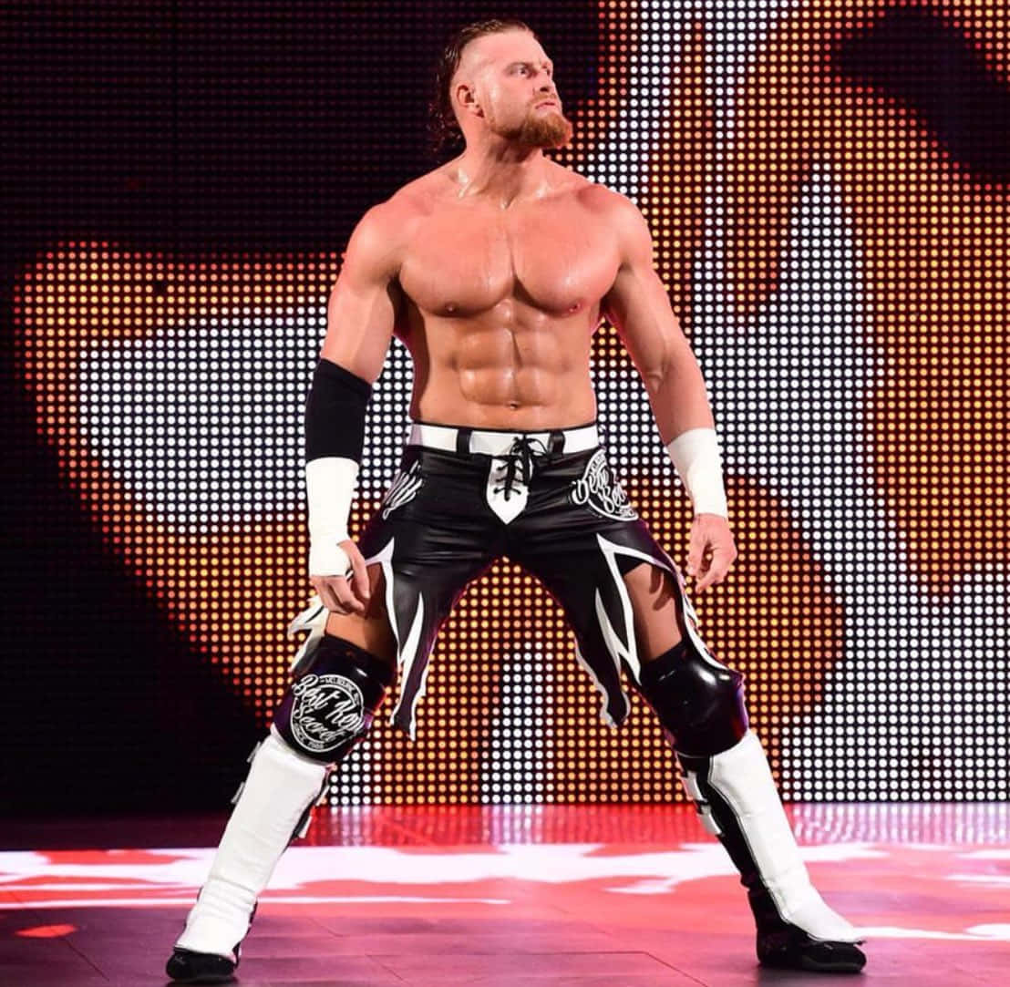 WWE 桌布 壁紙 — 一位肌肉發達的摔角手穿著黑白裝備，自信地站在一個有像素化橙色背景的燈光舞台上。