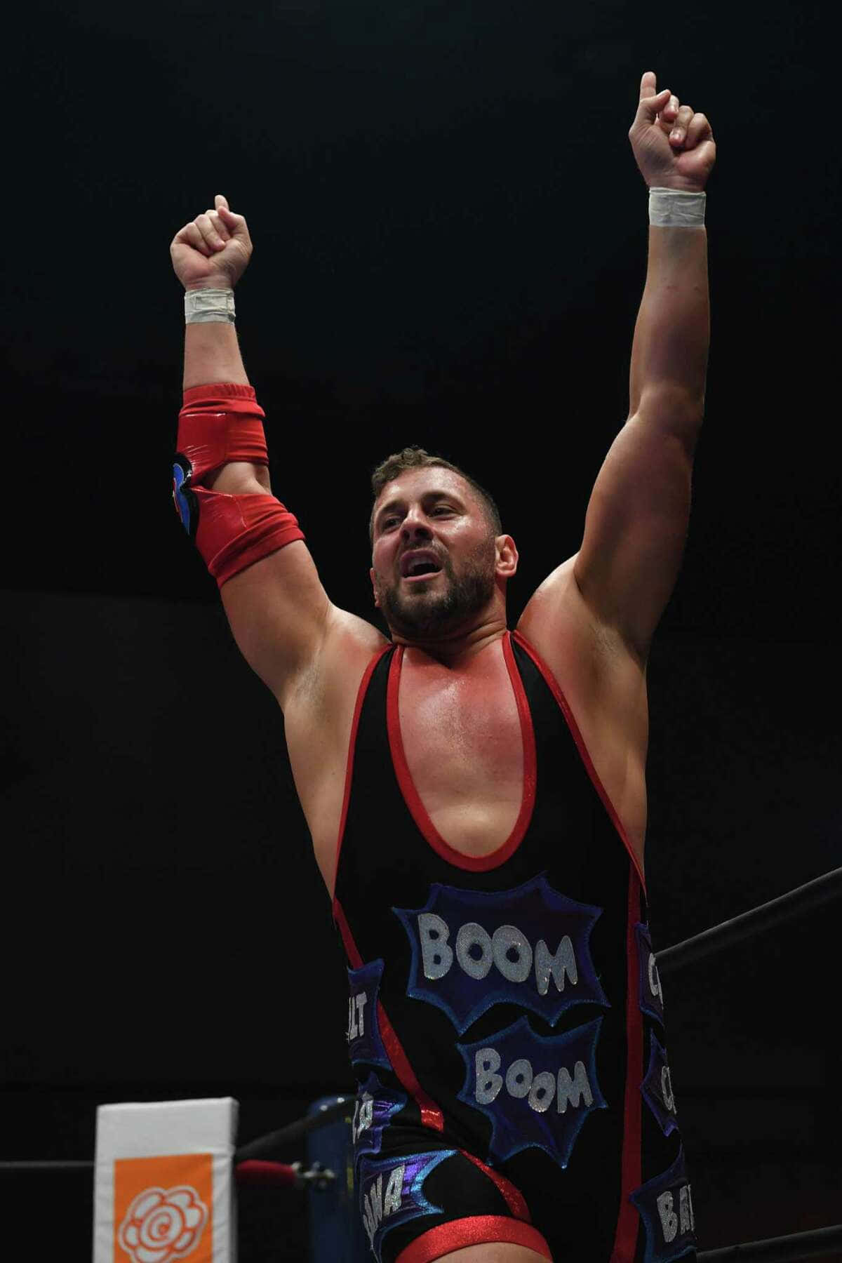 Colt Cabana 桌布 壁紙 — 一位肌肉發達的摔角手穿著黑紅色的「Boom Boom」緊身衣，在明亮的燈光下於擂台上高舉雙拳慶祝勝利。