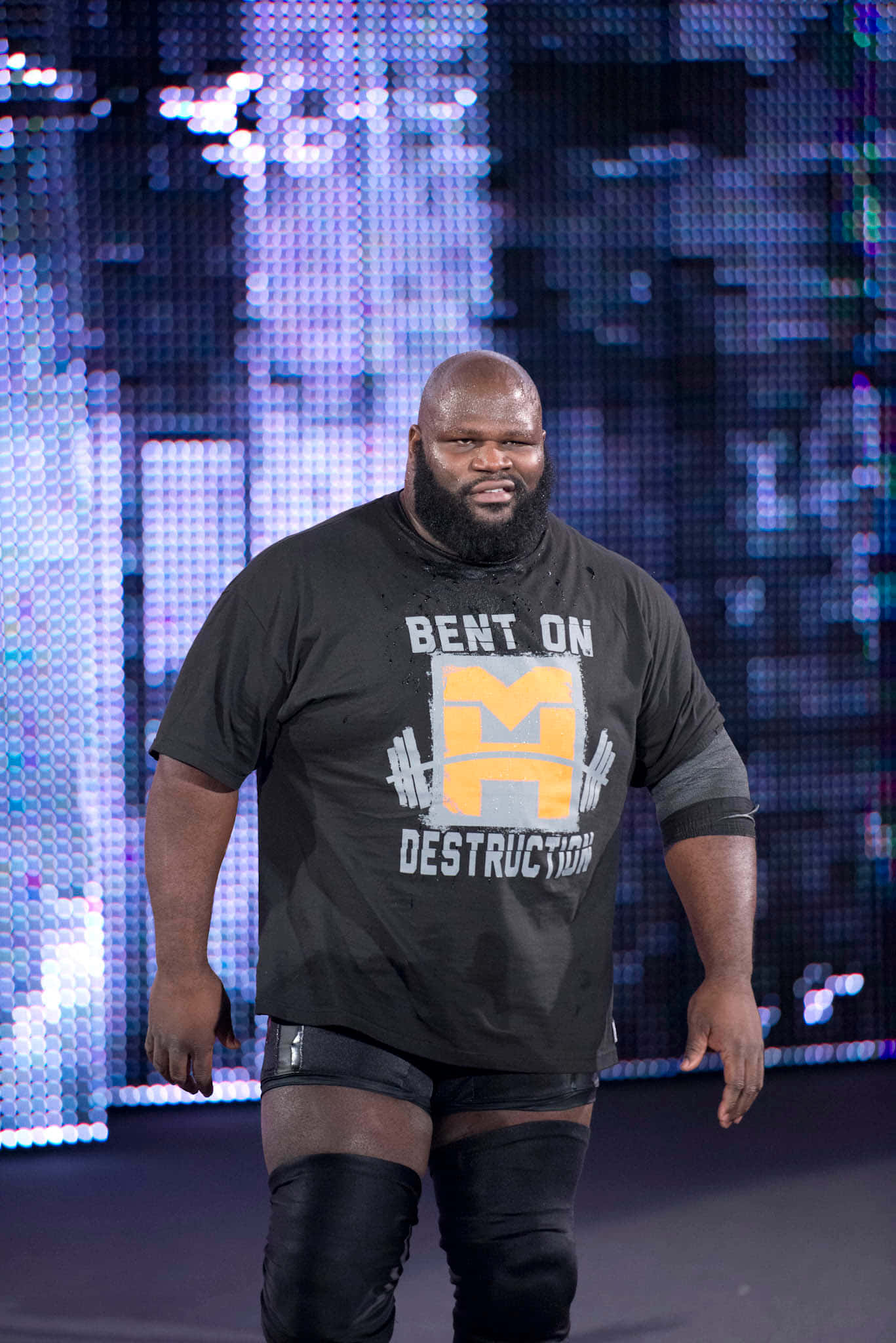 WWE 桌布 壁紙 — 一位肌肉發達的摔角手穿著黑色「Bent on Destruction」T恤，自信地走在帶有發光像素背景的舞台上。
