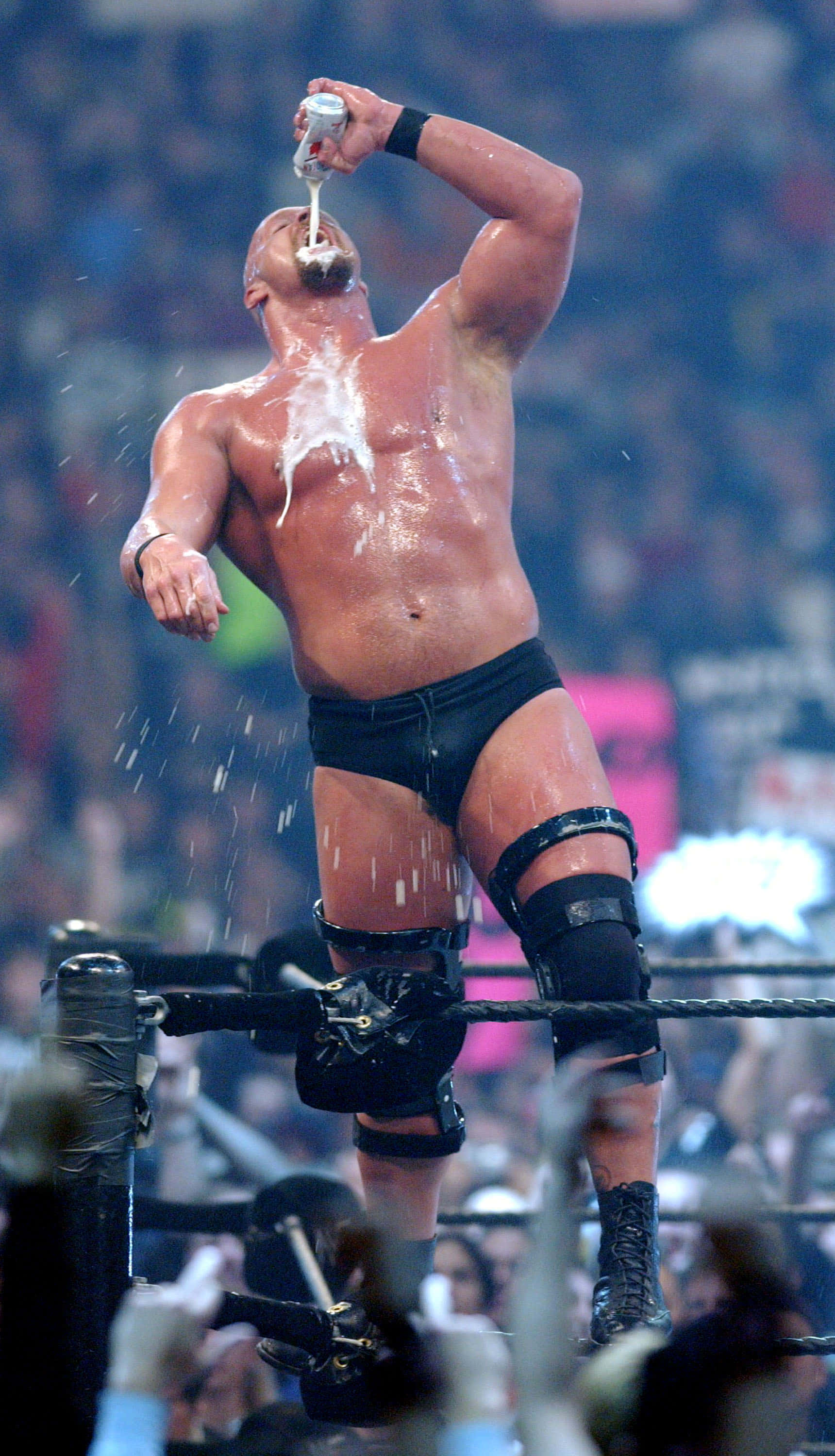 WWE 桌布 壁紙 — 一位肌肉發達的摔角手穿著黑色緊身褲站在擂台上，將一罐啤酒倒在自己頭上，液體四處飛濺。