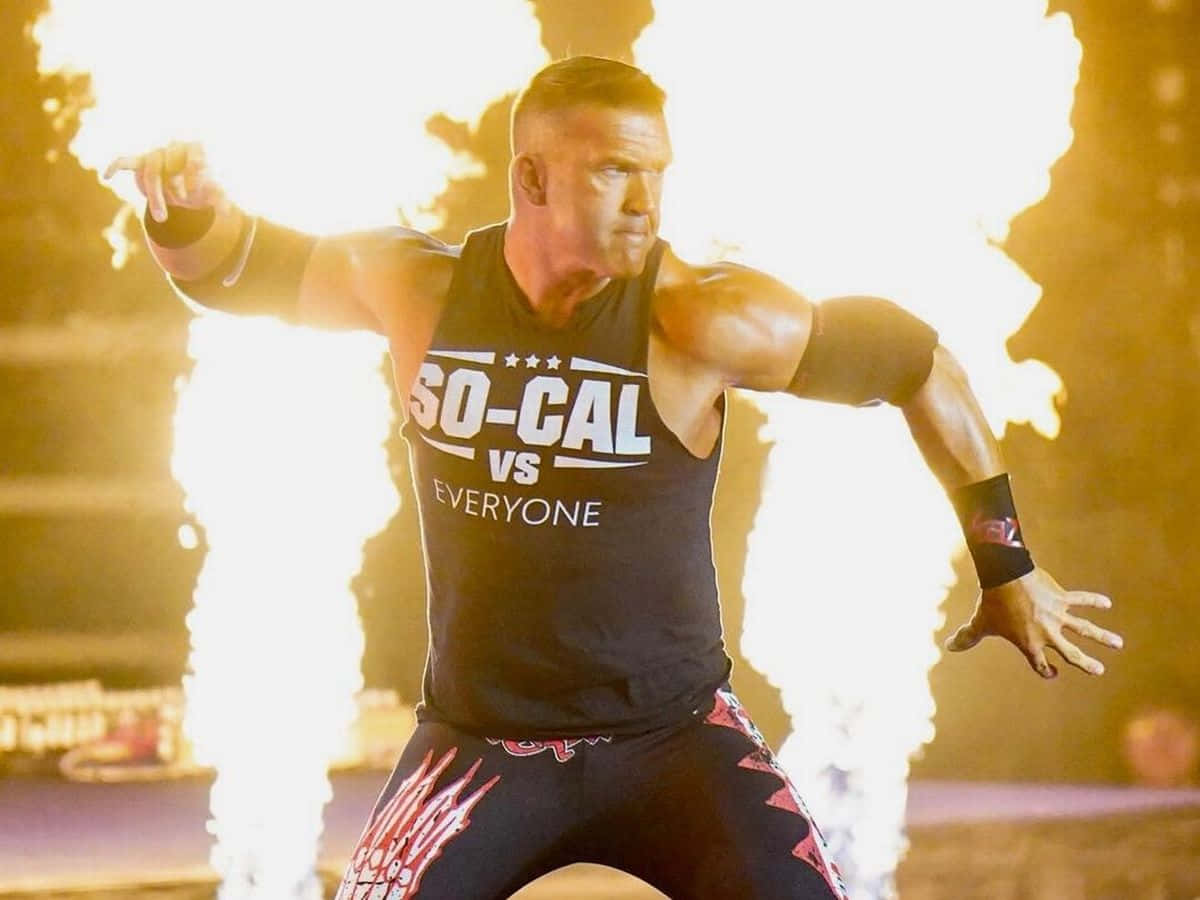 Flame 桌布 壁紙 — 一位肌肉發達的摔角手身穿印有「SO-CAL VS EVERYONE」的黑色背心，張開雙臂向前邁進，身後爆發熾熱的爆炸。