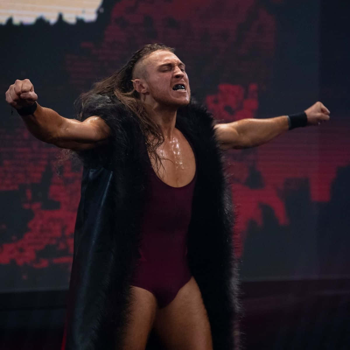 WWE 桌布 壁紙 — 一位肌肉發達的摔角手身穿栗色緊身衣和黑色毛皮披風，在摔角台上張開雙臂勝利地吶喊。