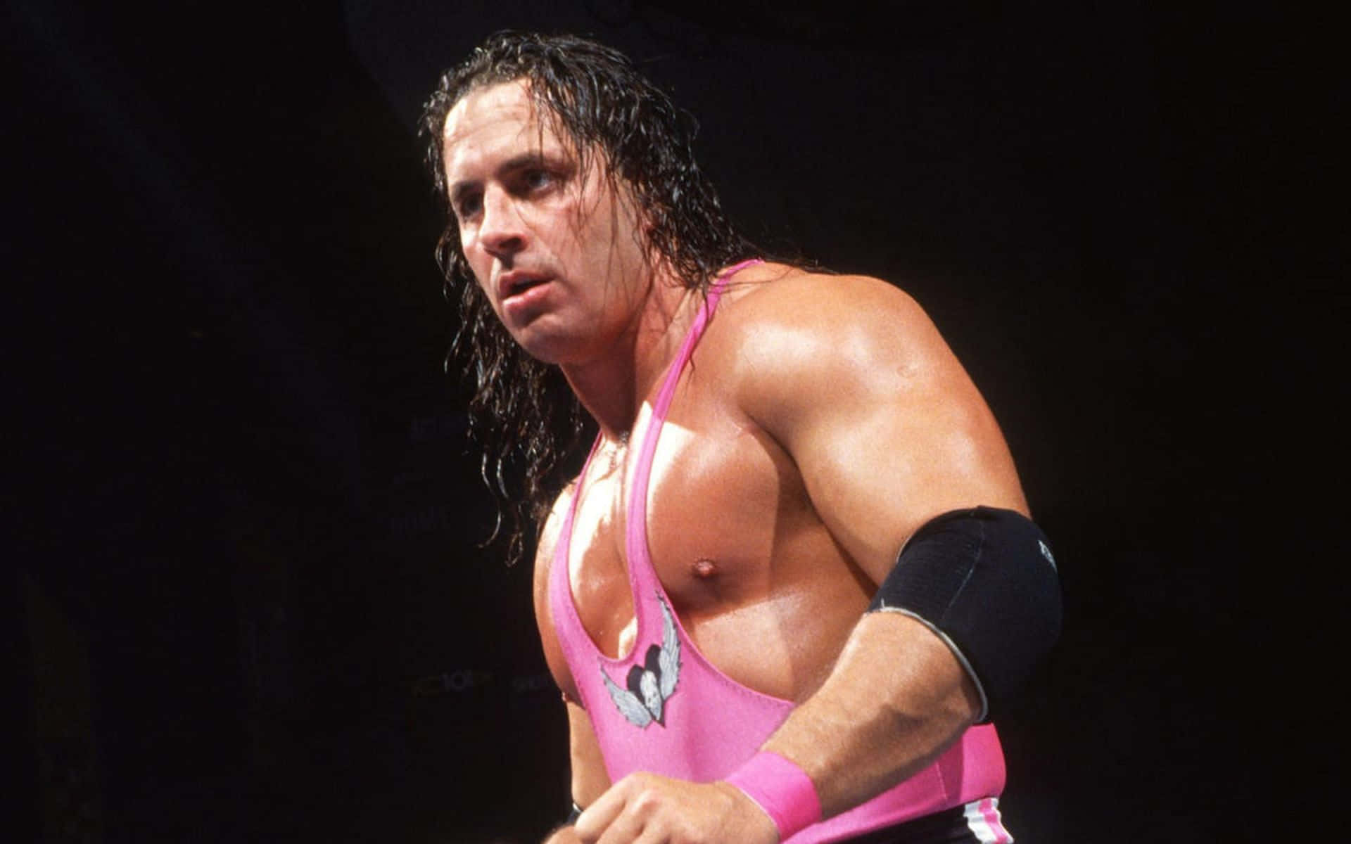 WWE 桌布 壁紙 — 一位肌肉發達的摔角手身穿粉紅色緊身衣，濕髮和黑色護肘，在黑暗背景下凝視著。