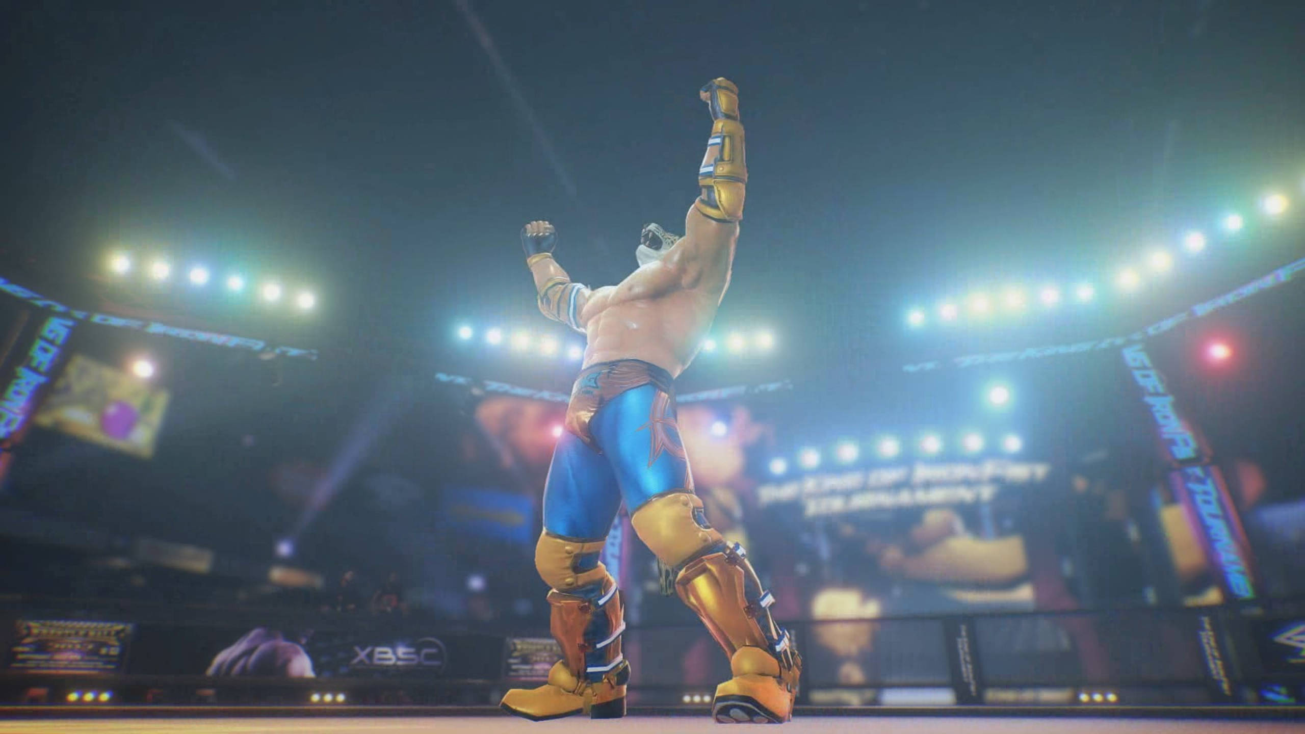 Tekken 桌布 壁紙 — 一位肌肉發達的摔角手身穿藍色和金色裝備，在體育場燈光下明亮的競技場中勝利地高舉雙臂。
