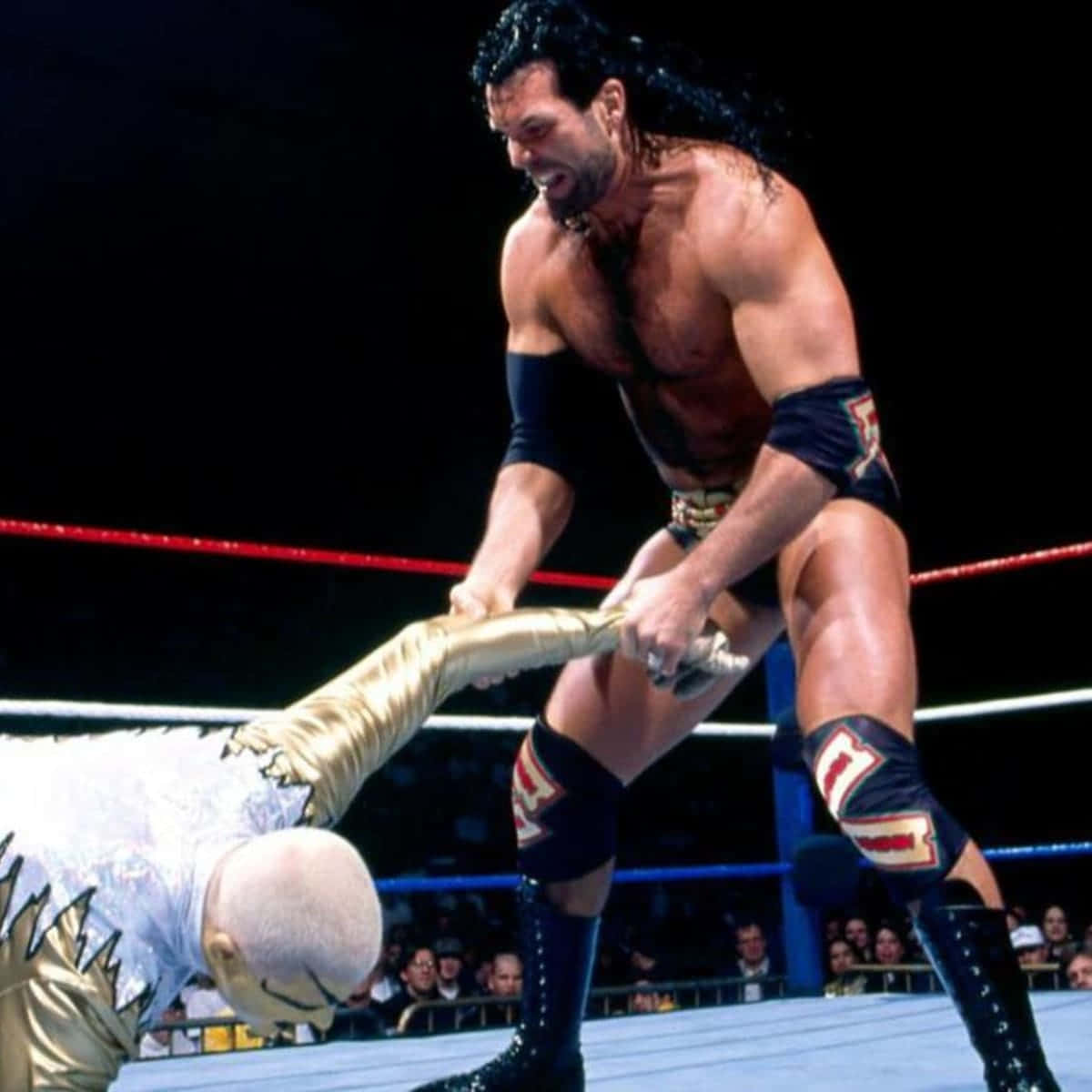 WWE 桌布 壁紙 — 一位肌肉發達的摔角手身穿黑色裝備，在燈光明亮的擂台上壓制對手，背景是咆哮的粉絲。