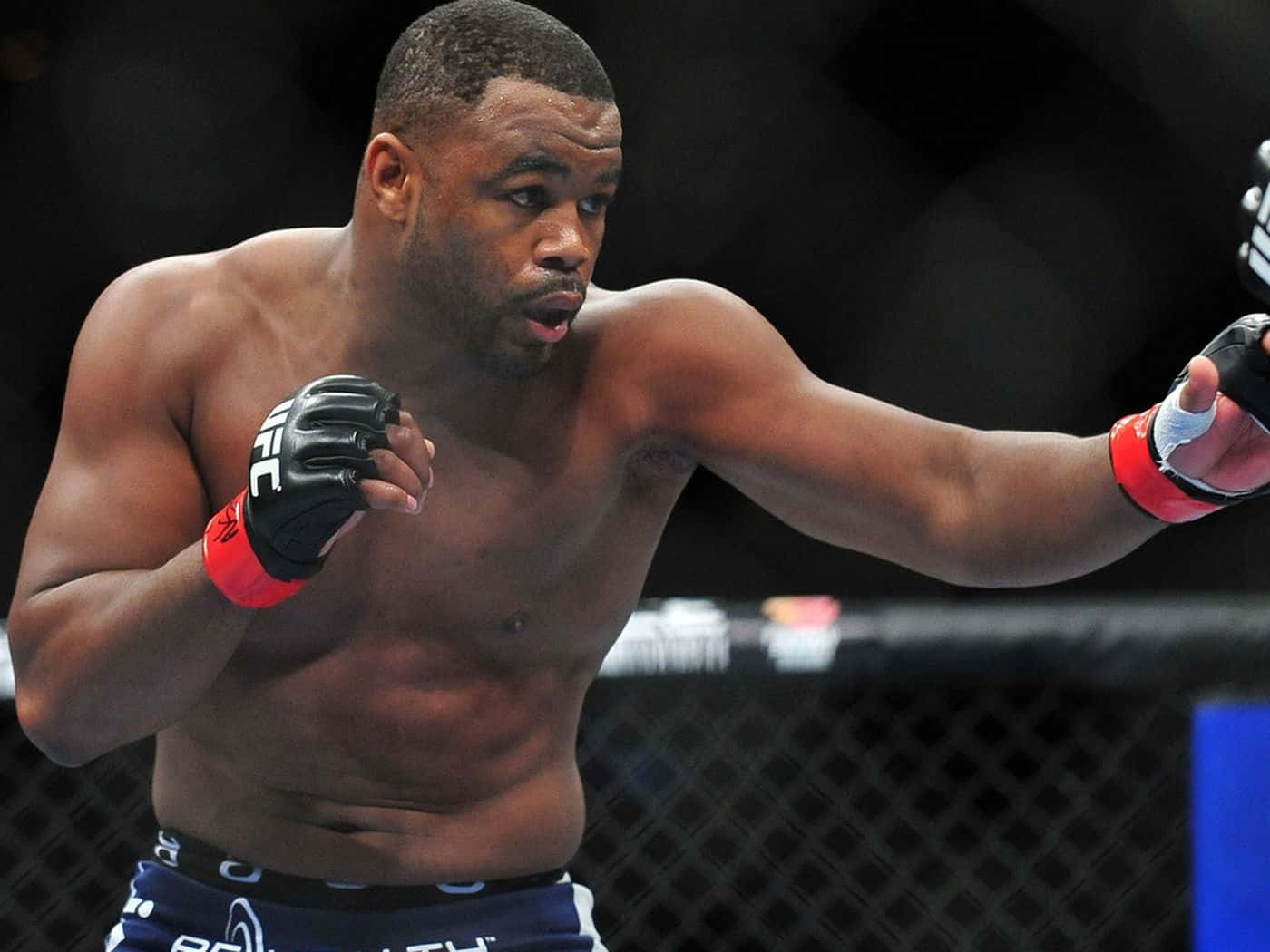 UFC 桌布 壁紙 — 一位肌肉發達的混合武術選手在昏暗的八角籠內，於UFC比賽中揮出強力一拳。