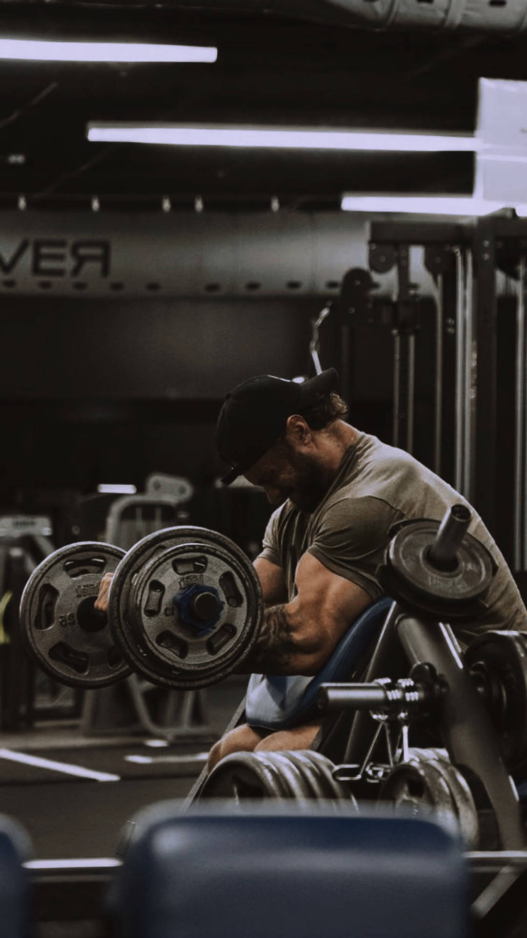 Exercise 桌布 壁紙 — 一位肌肉發達的男子在健身房中，在明亮的螢光燈下，專注地舉起沉重的啞鈴。