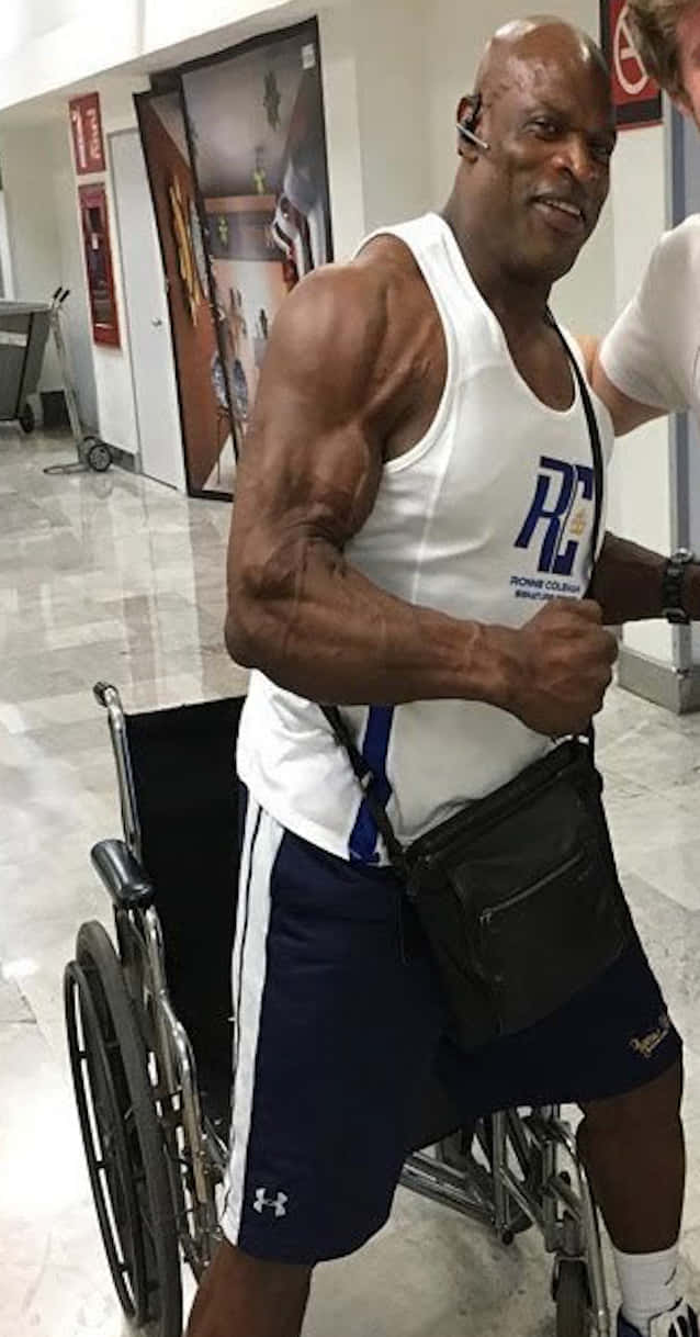 運動 桌布 壁紙 — 一位肌肉發達的男子坐在輪椅上，在光線明亮的室內走廊彎曲肱二頭肌。