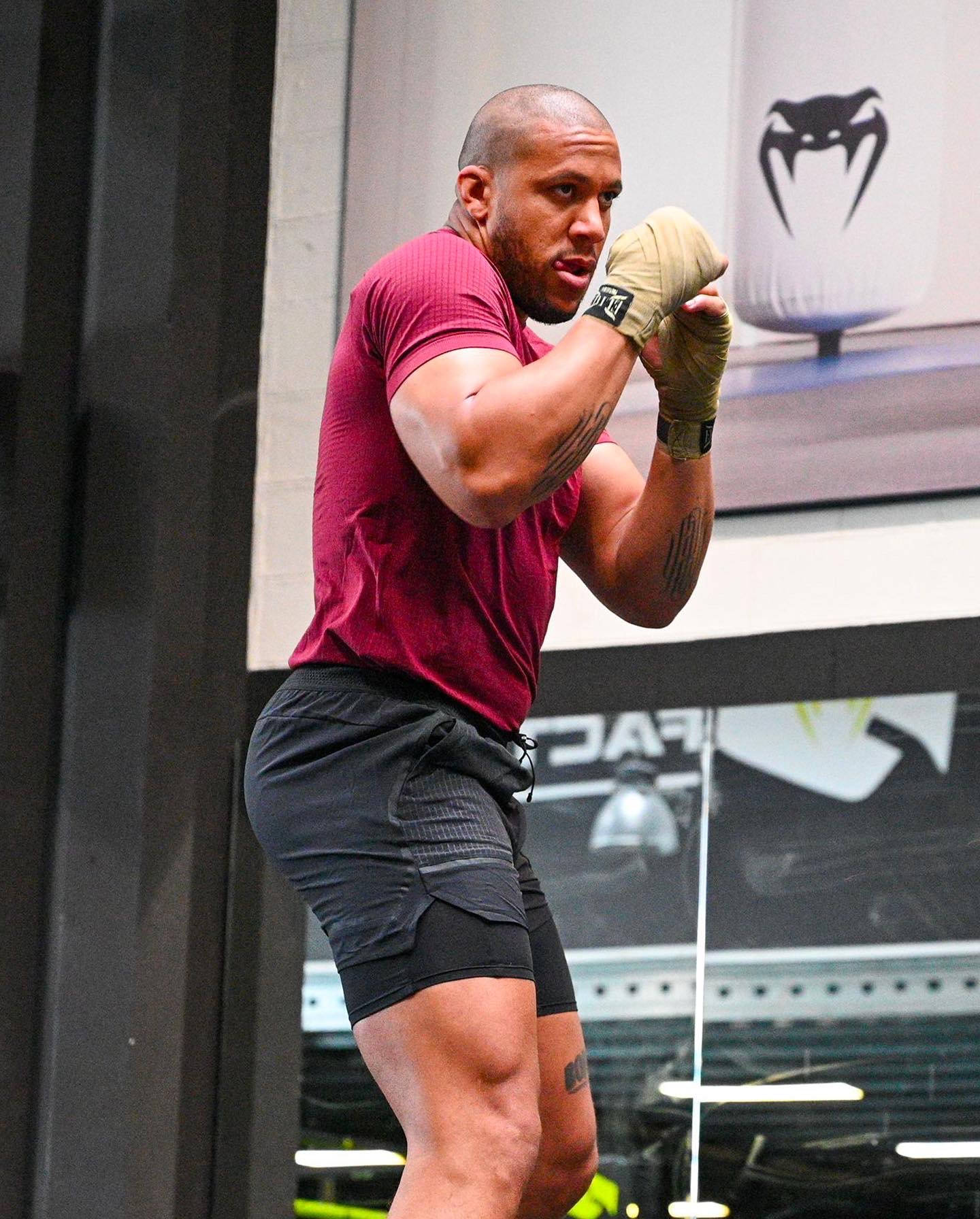 MMA 桌布 壁紙 — 一位肌肉發達的男子穿著紅色襯衫和黑色短褲，在現代健身房中用纏繞的手進行高強度訓練。
