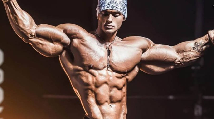 Exercise 桌布 壁紙 — 一位肌肉發達的男性健美運動員在戲劇性的舞台燈光下，戴著圖案頭帶，繃緊手臂和軀幹。
