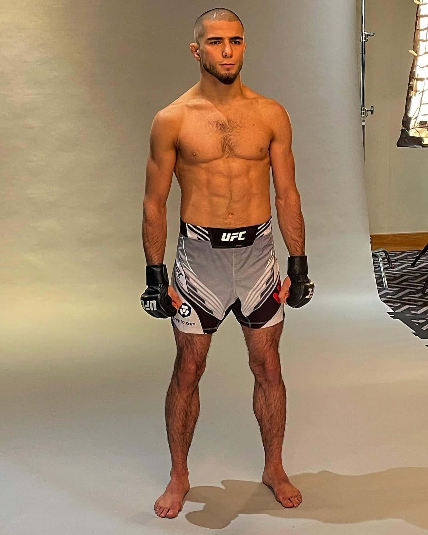 MMA 桌布 壁紙 — 一位肌肉發達的男性拳手穿著UFC短褲和手套，赤腳站在一個光線中性且設備可見的攝影棚中。
