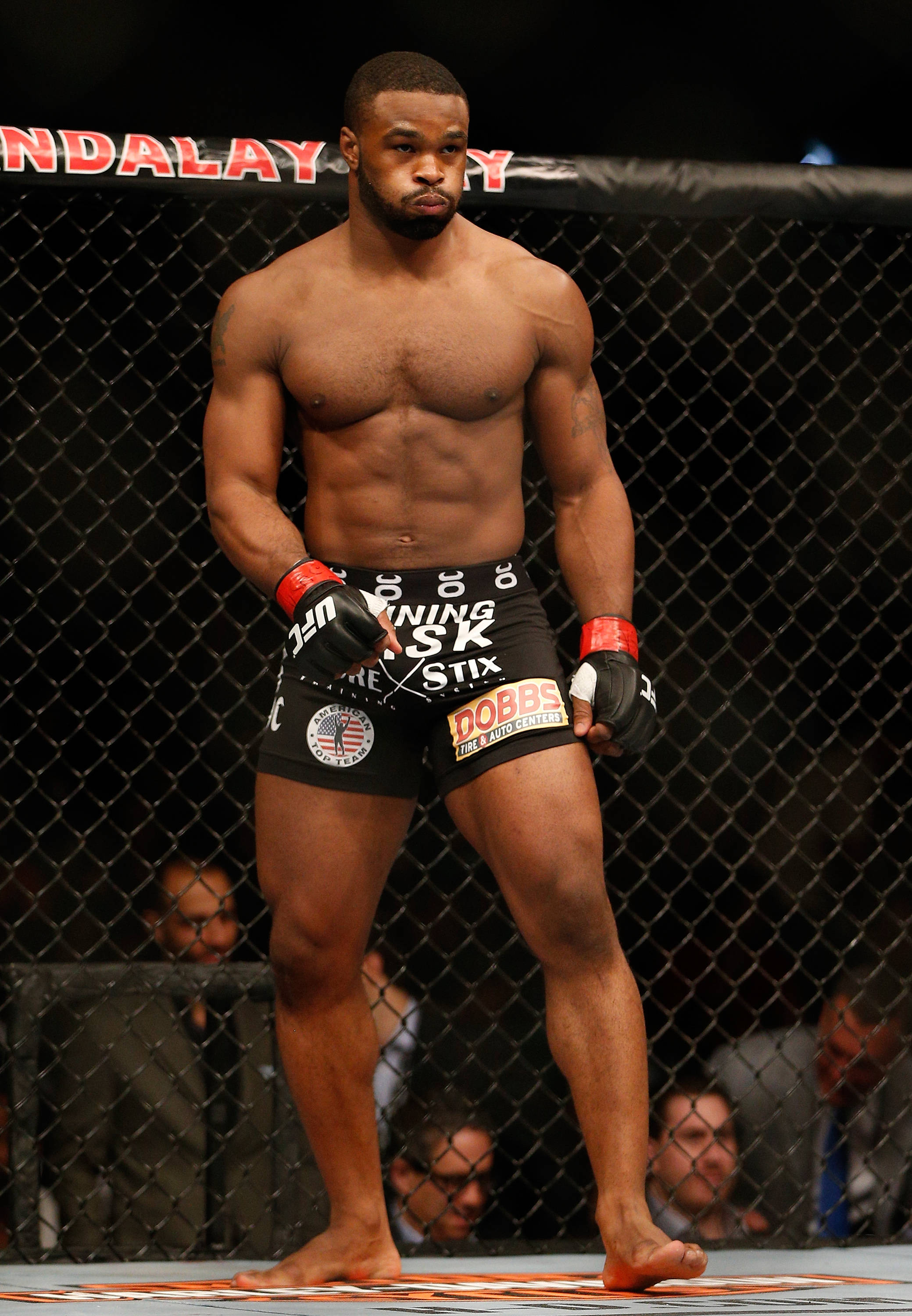 Tyron Woodley 桌布 壁紙 — 一位肌肉發達的男性拳手赤腳站在UFC八角籠內，穿著黑色短褲和手套，神情專注。