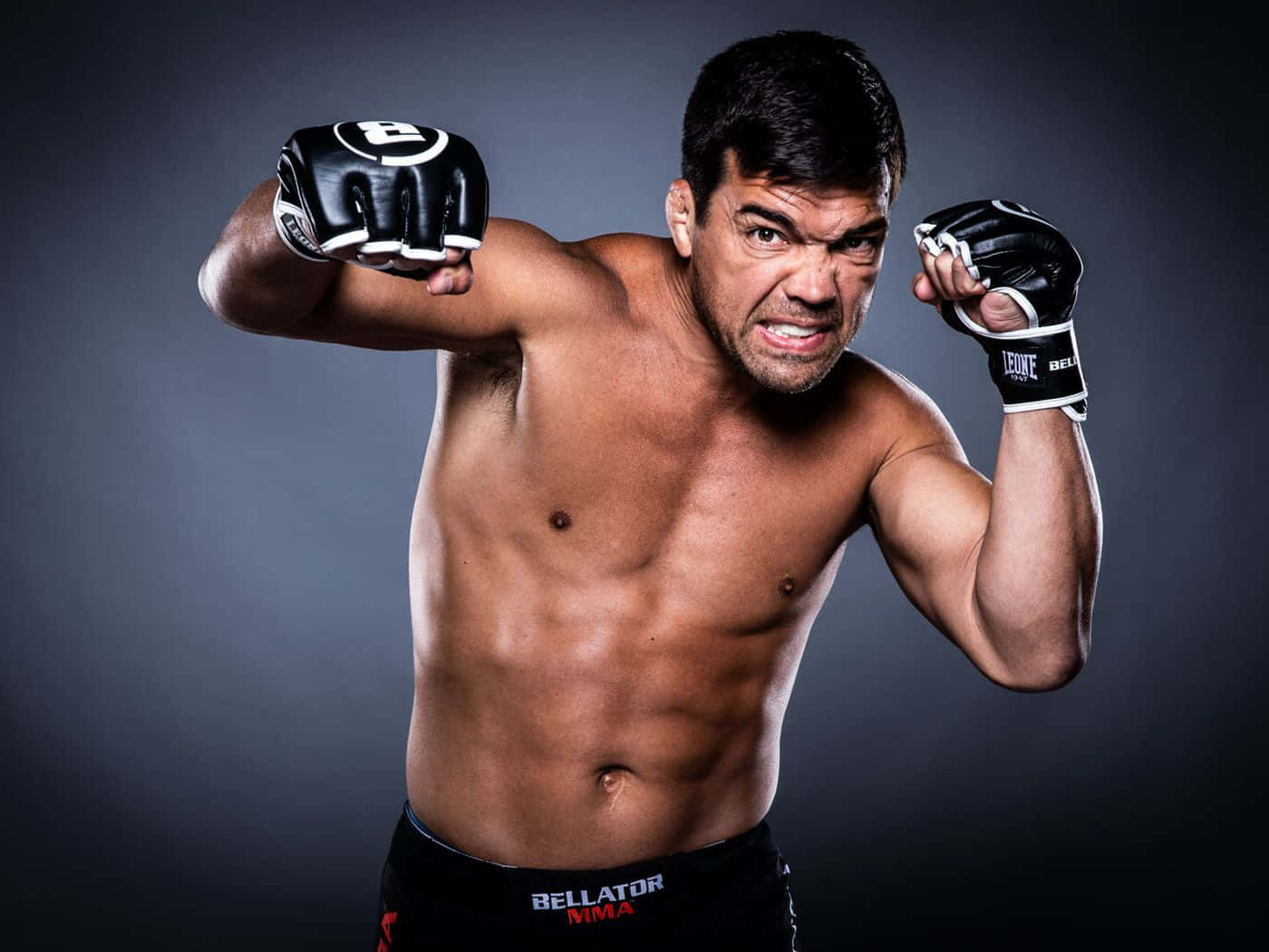 21:9 桌布 壁紙 — 一位肌肉發達的男性拳擊手，戴著黑色手套和Bellator短褲，在深灰色工作室背景前擺出挑釁姿勢。