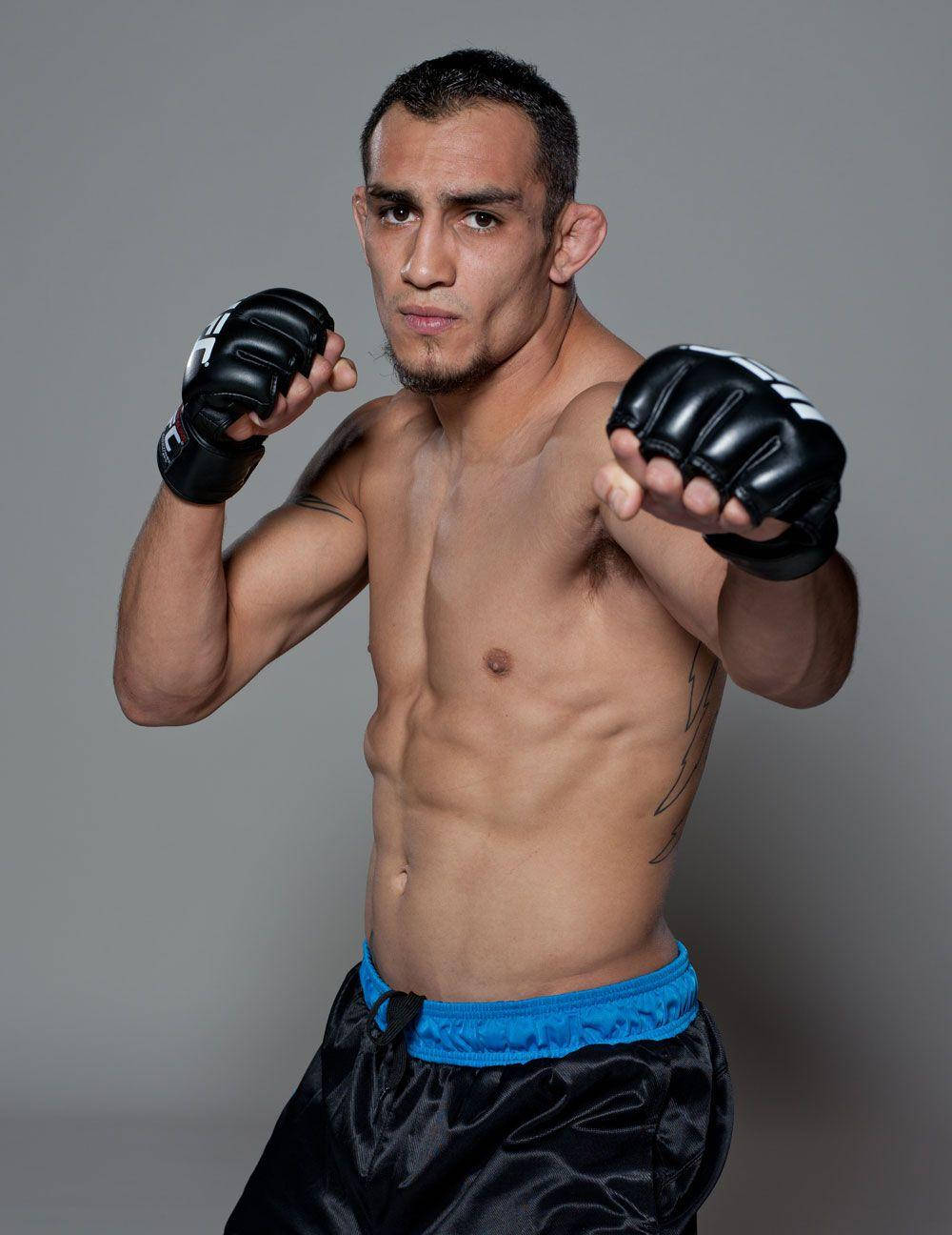 MMA 桌布 壁紙 — 一位肌肉發達的男性拳擊手戴著黑色手套和藍色鑲邊短褲，在純灰色工作室背景前擺出專注的戰鬥姿勢。