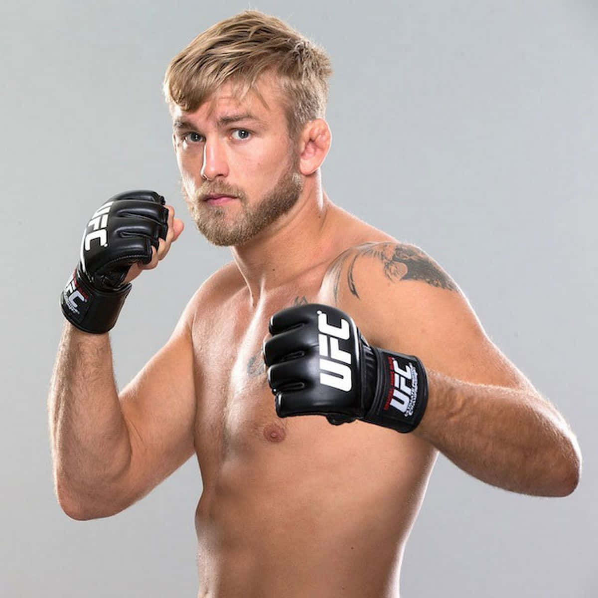 UFC 桌布 壁紙 — 一位肌肉發達的男性拳擊手戴著黑色UFC手套，在純灰色工作室背景下擺出專注的表情。