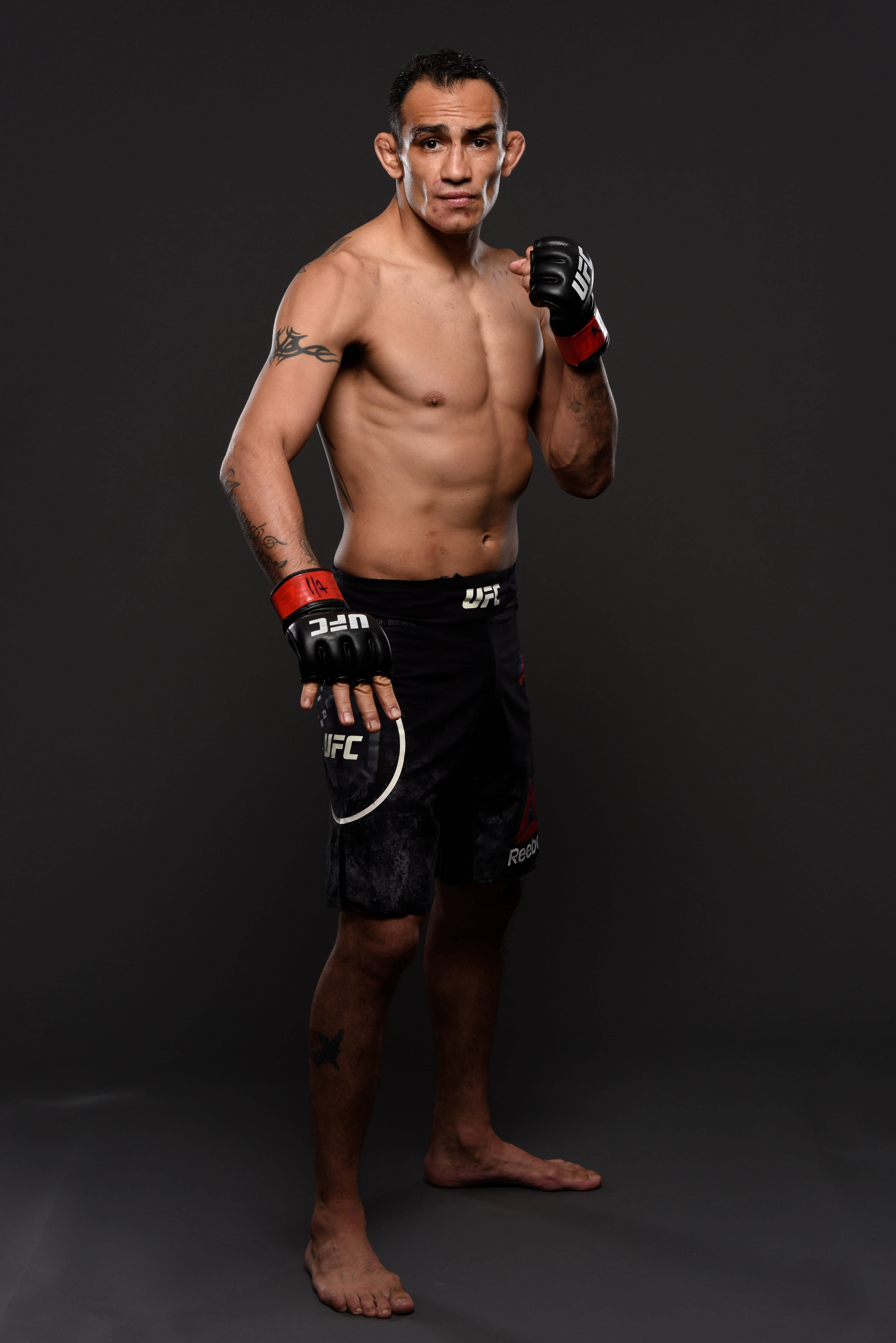 黑色 桌布 壁紙 — 一位肌肉發達的男性混合武術家穿著UFC裝備，赤腳站在黑暗的攝影棚背景前，表情專注。
