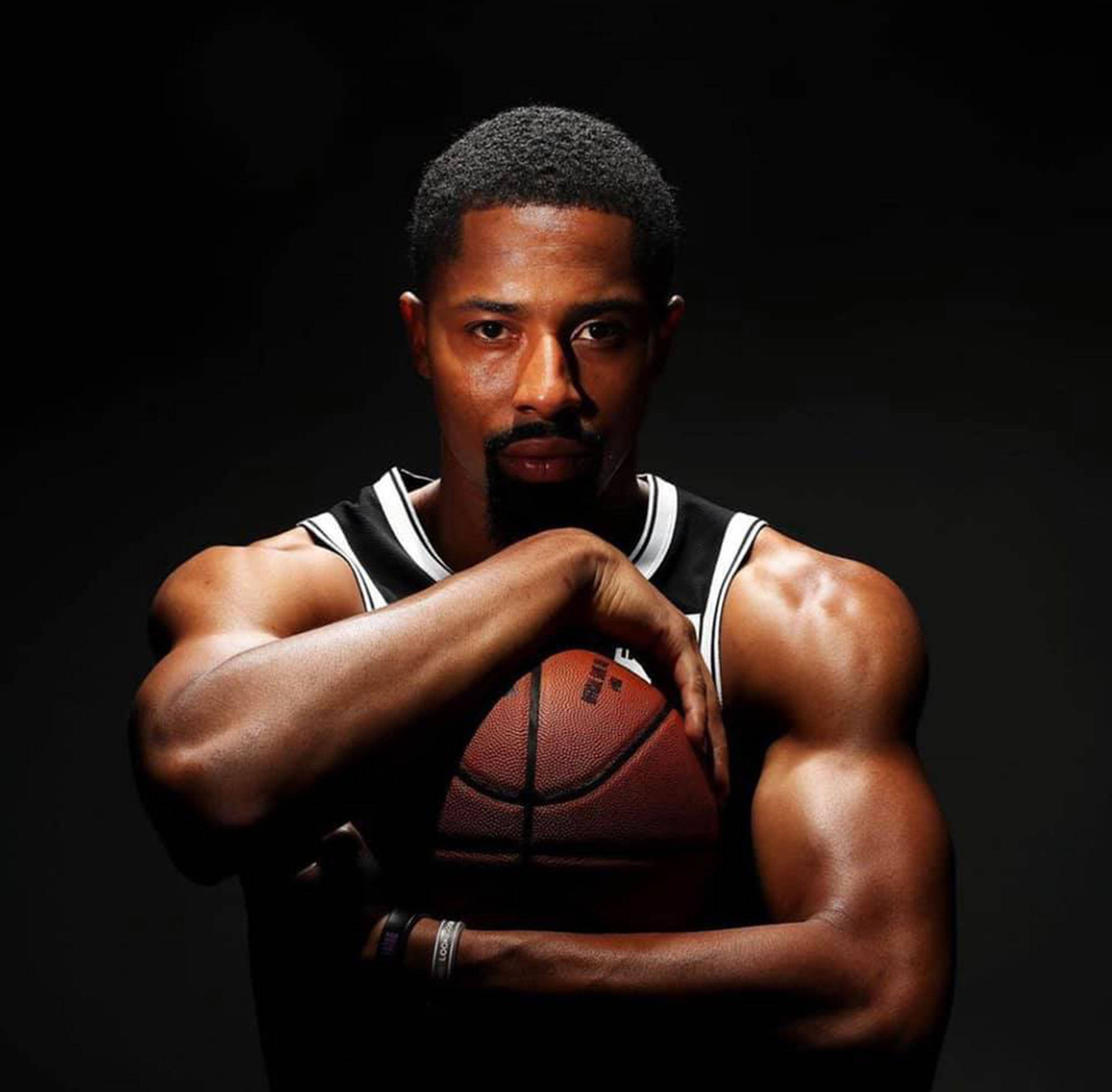 spencer dinwiddie 桌布 壁紙 — 一位肌肉發達的籃球運動員穿著黑白球衣，在戲劇性燈光的黑暗背景下持球。